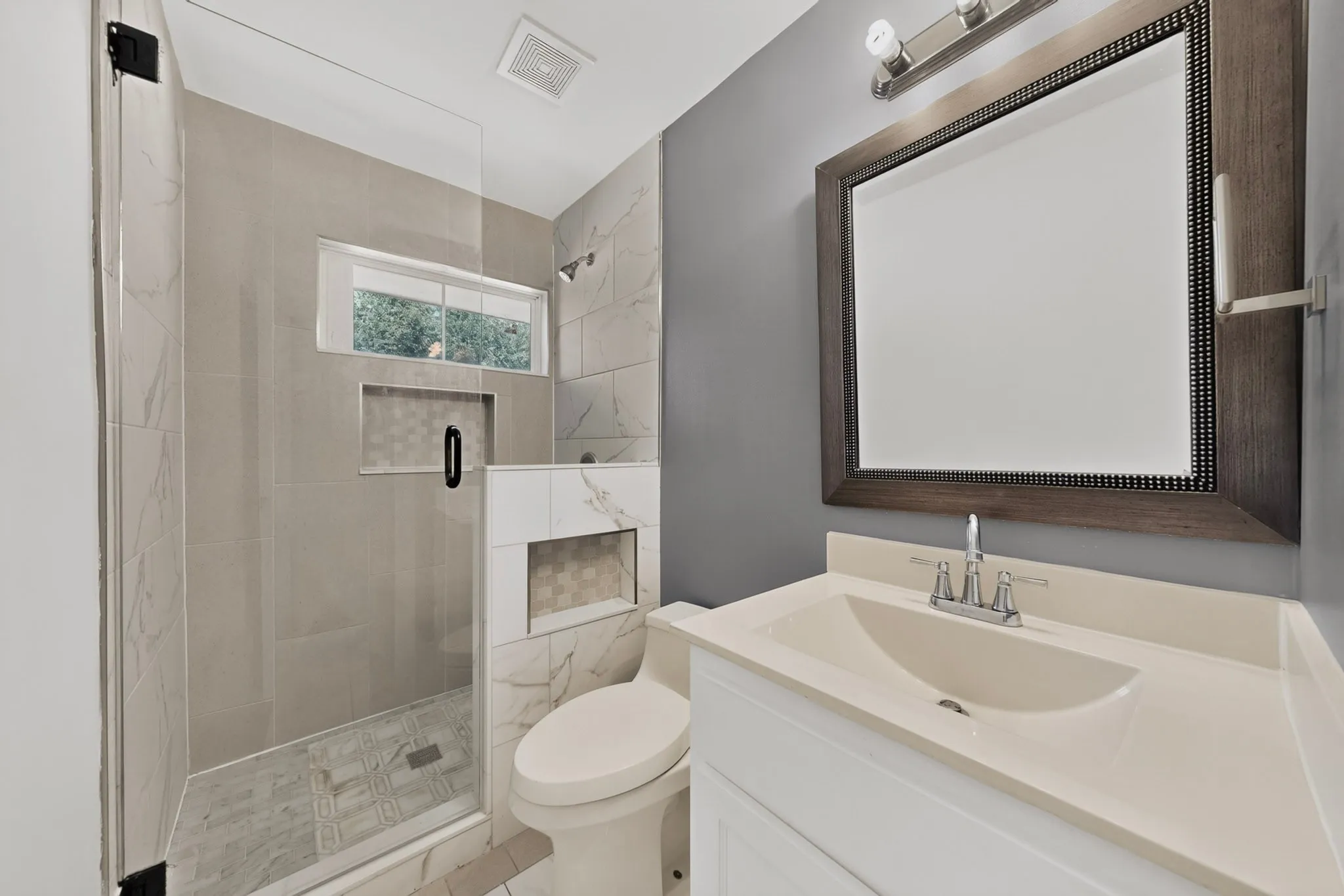 Bathroom featuring a glass-enclosed shower with tile surround, integrated shower niche, and a frosted window