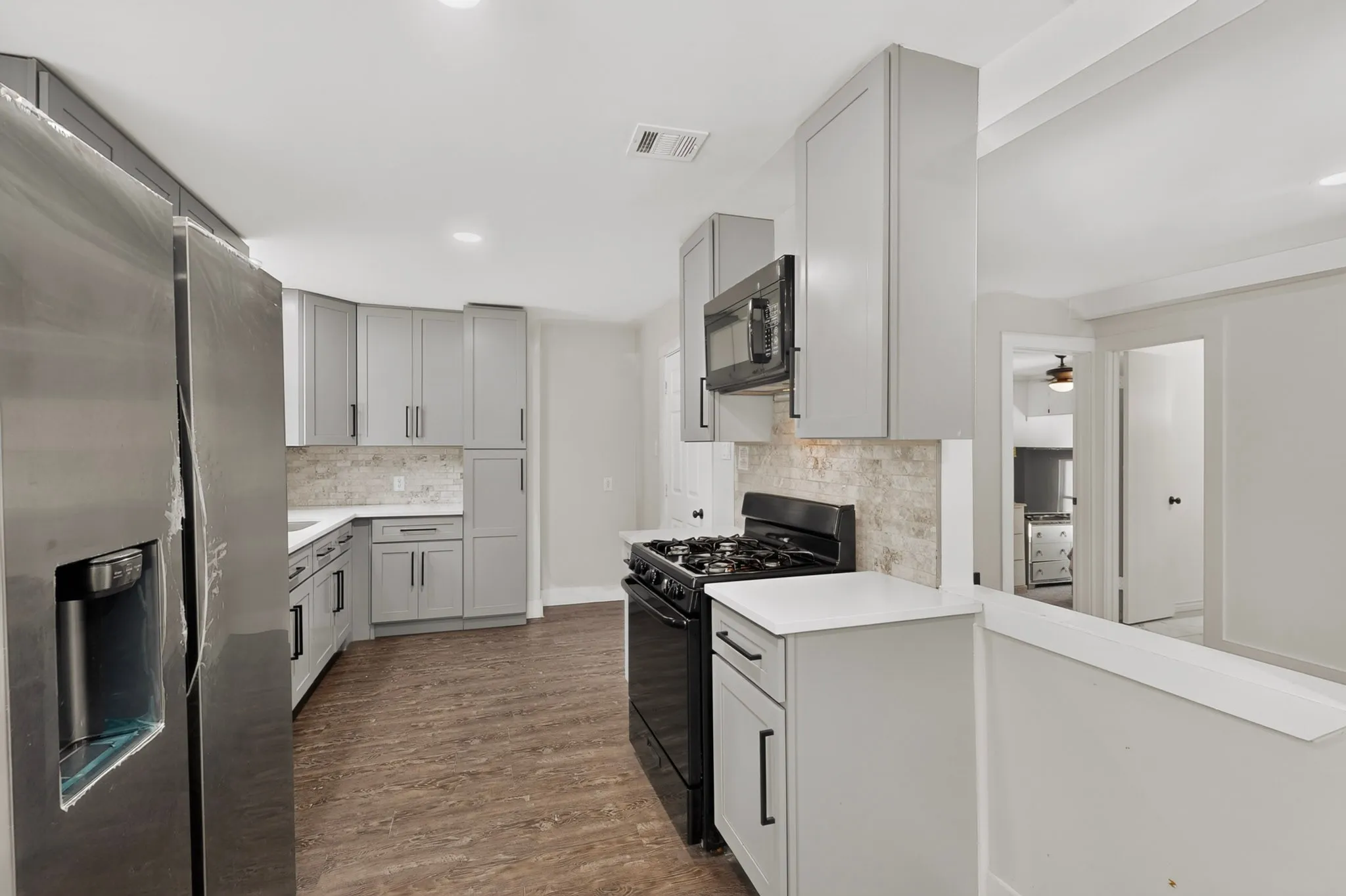 Bright kitchen featuring light gray cabinetry with dark hardware, white countertops, a tiled backsplash, wood-finish flooring, and stainless steel appliances