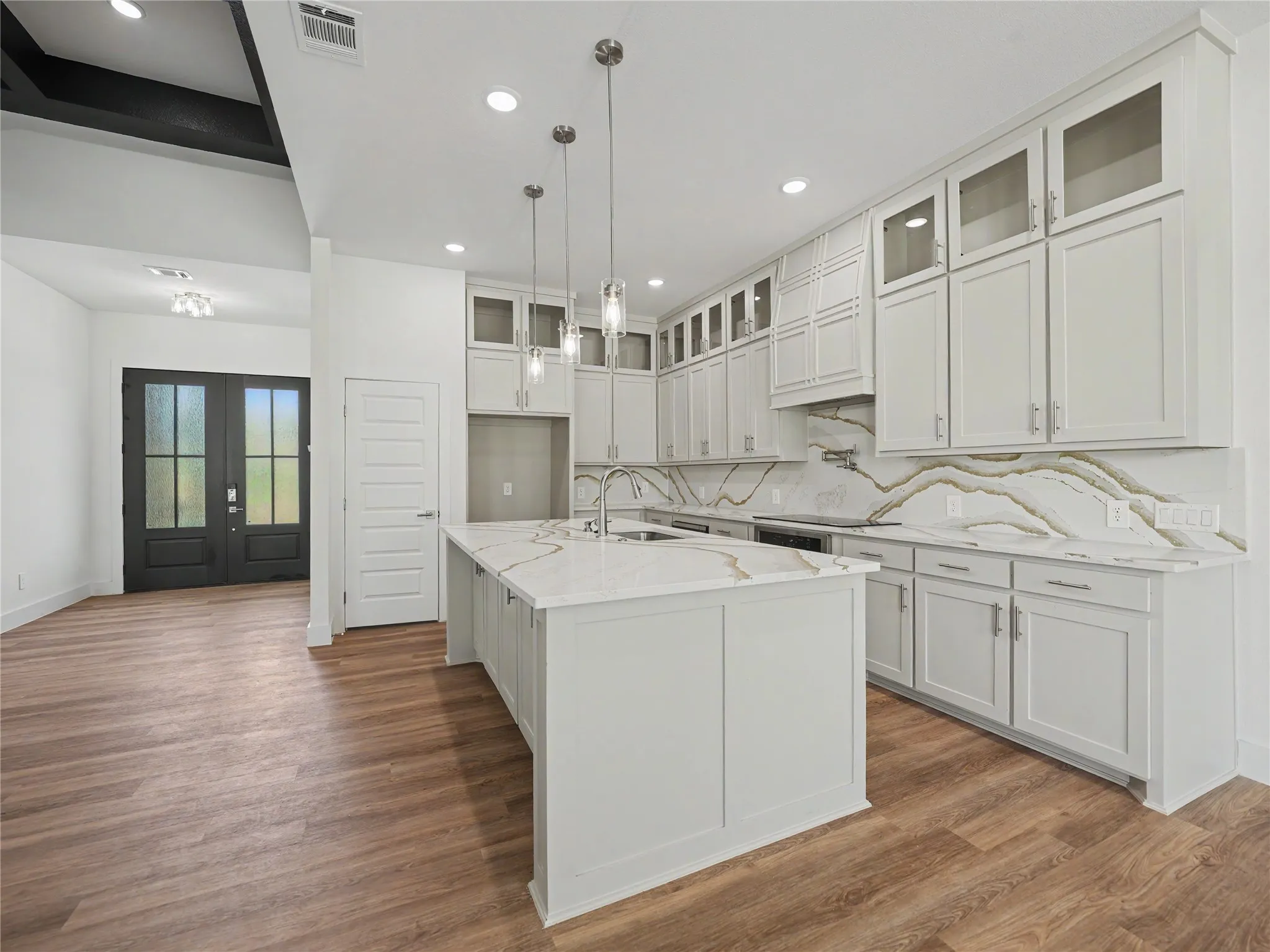 Contemporary kitchen featuring an island with a sink, white cabinetry, integrated appliances, and a marble-patterned backsplash