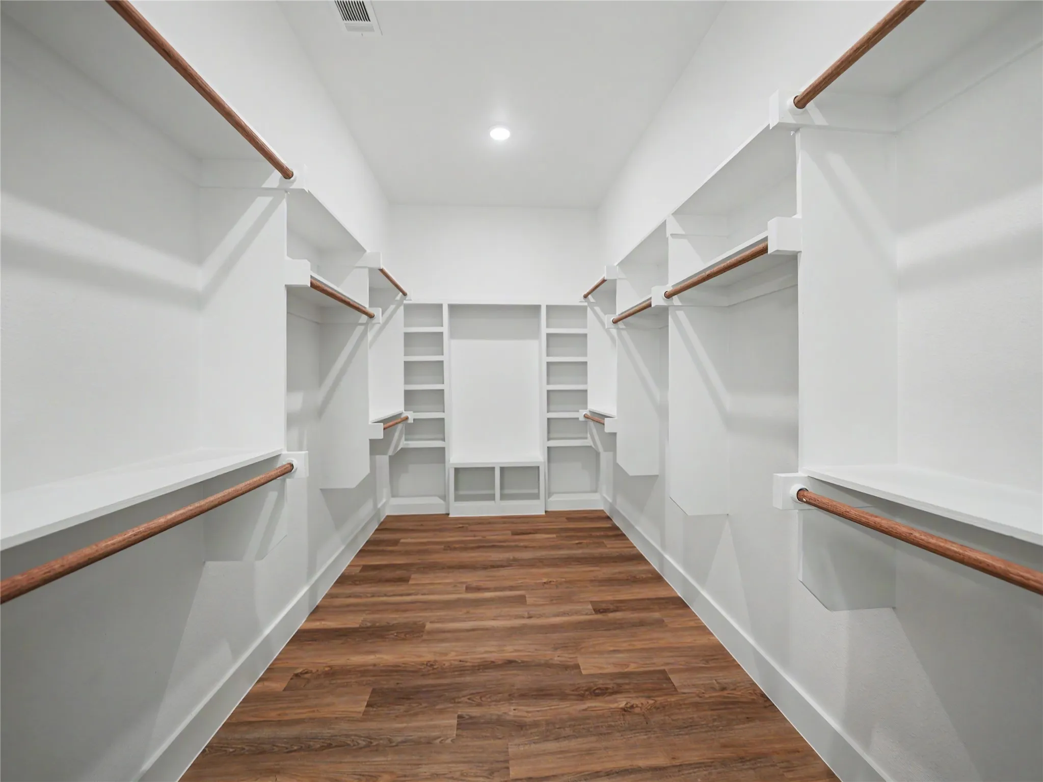 Spacious walk-in closet featuring wood-finish flooring, extensive built-in shelving, multiple hanging rods, and recessed lighting