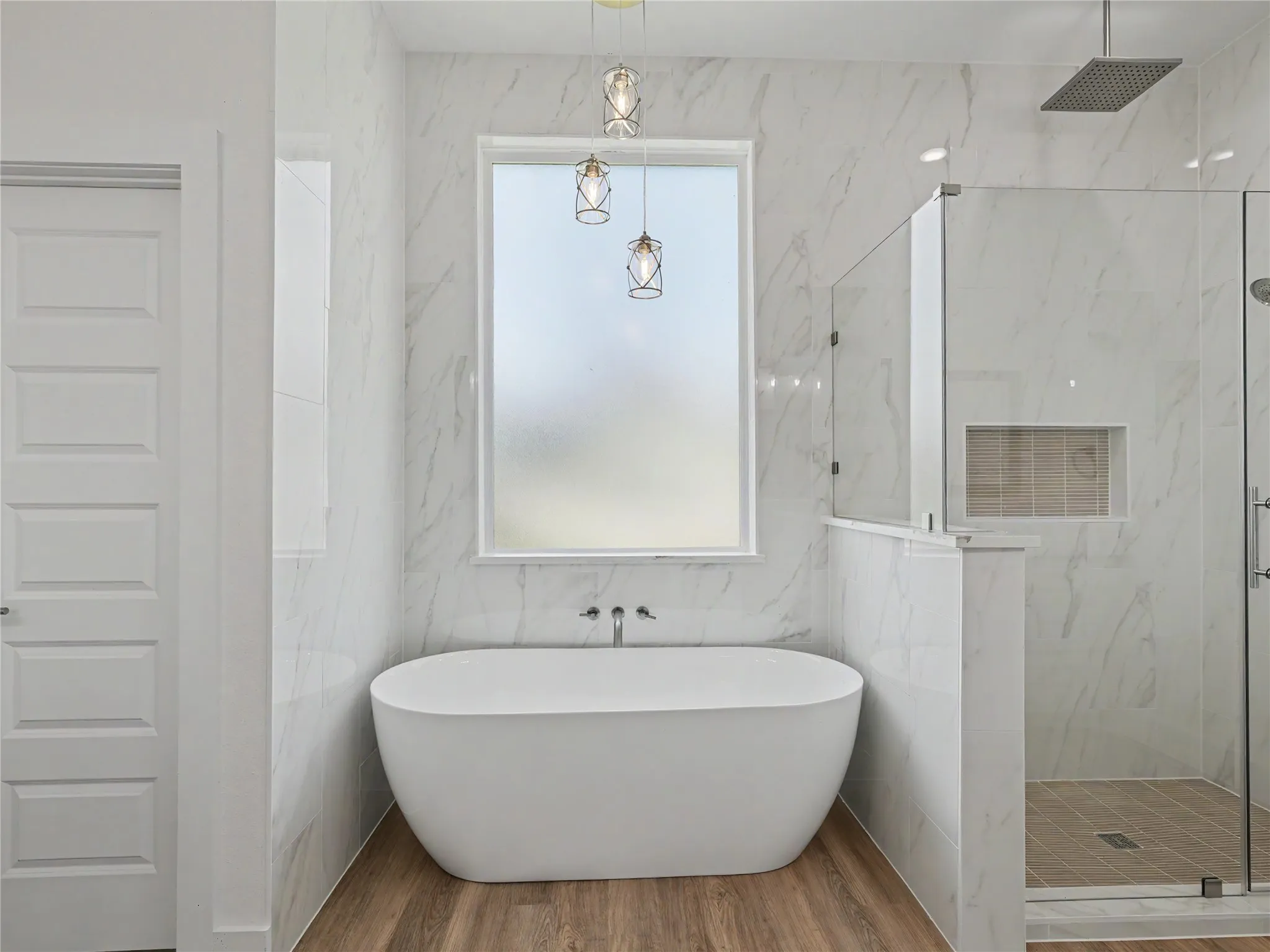 Spacious bathroom featuring a freestanding soaking tub with wall-mounted faucet, a walk-in shower with glass enclosure, and wood-finish flooring