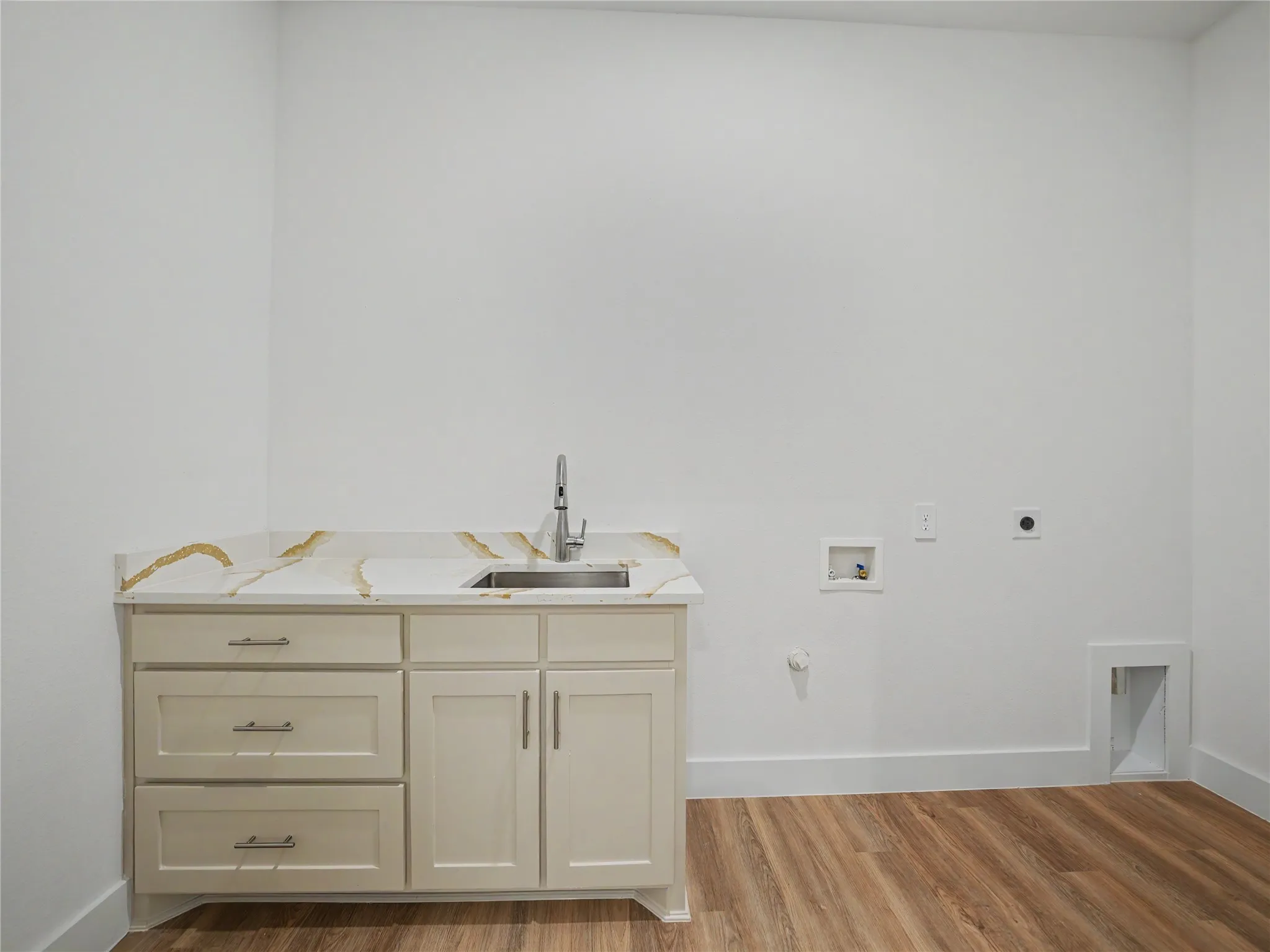 Laundry room featuring a utility sink with a stainless steel faucet, light-toned cabinetry, and a countertop with gold veining