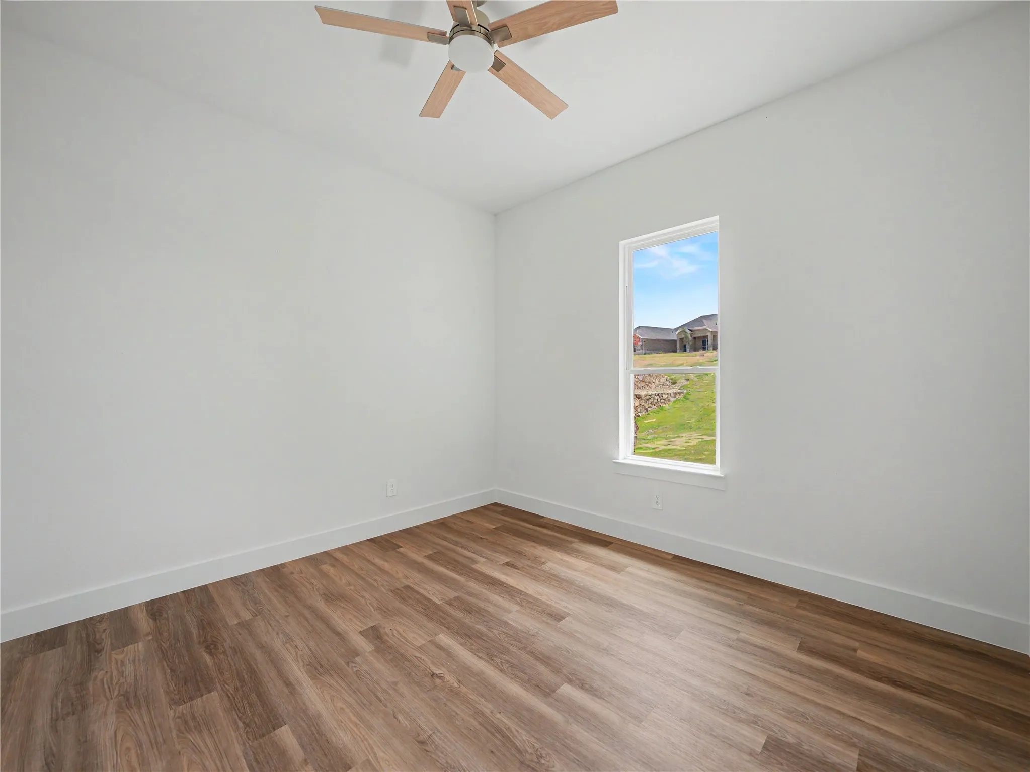 Room featuring wood-finish flooring, a single window, white walls, and a ceiling fan