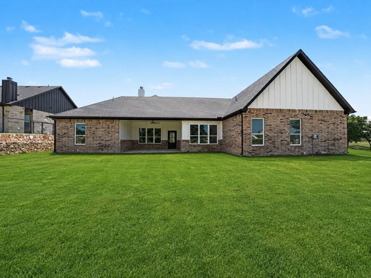 Expansive backyard featuring a manicured lawn, a covered patio with ceiling fan, and a brick exterior with white vertical siding accents