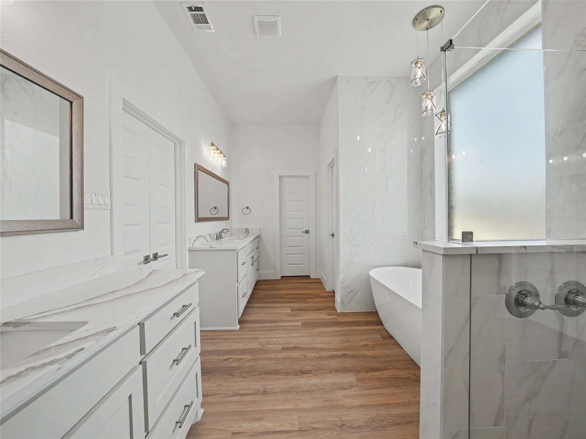 Contemporary bathroom featuring a freestanding tub, a walk-in shower with a frosted glass panel, and dual vanities with white cabinetry and light-toned countertops