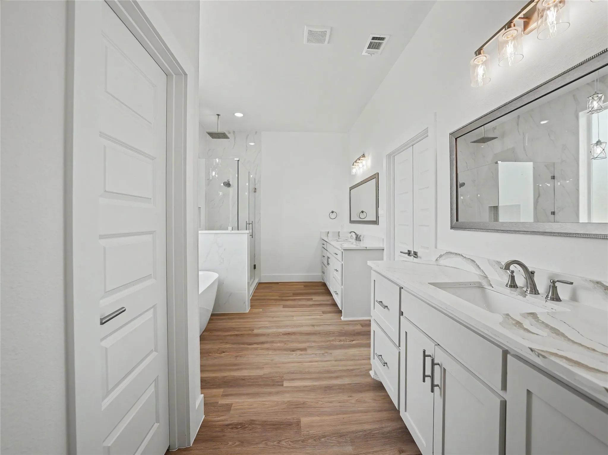 Spacious bathroom featuring wood-finish flooring, a freestanding tub, and a glass-enclosed shower with a rainfall showerhead