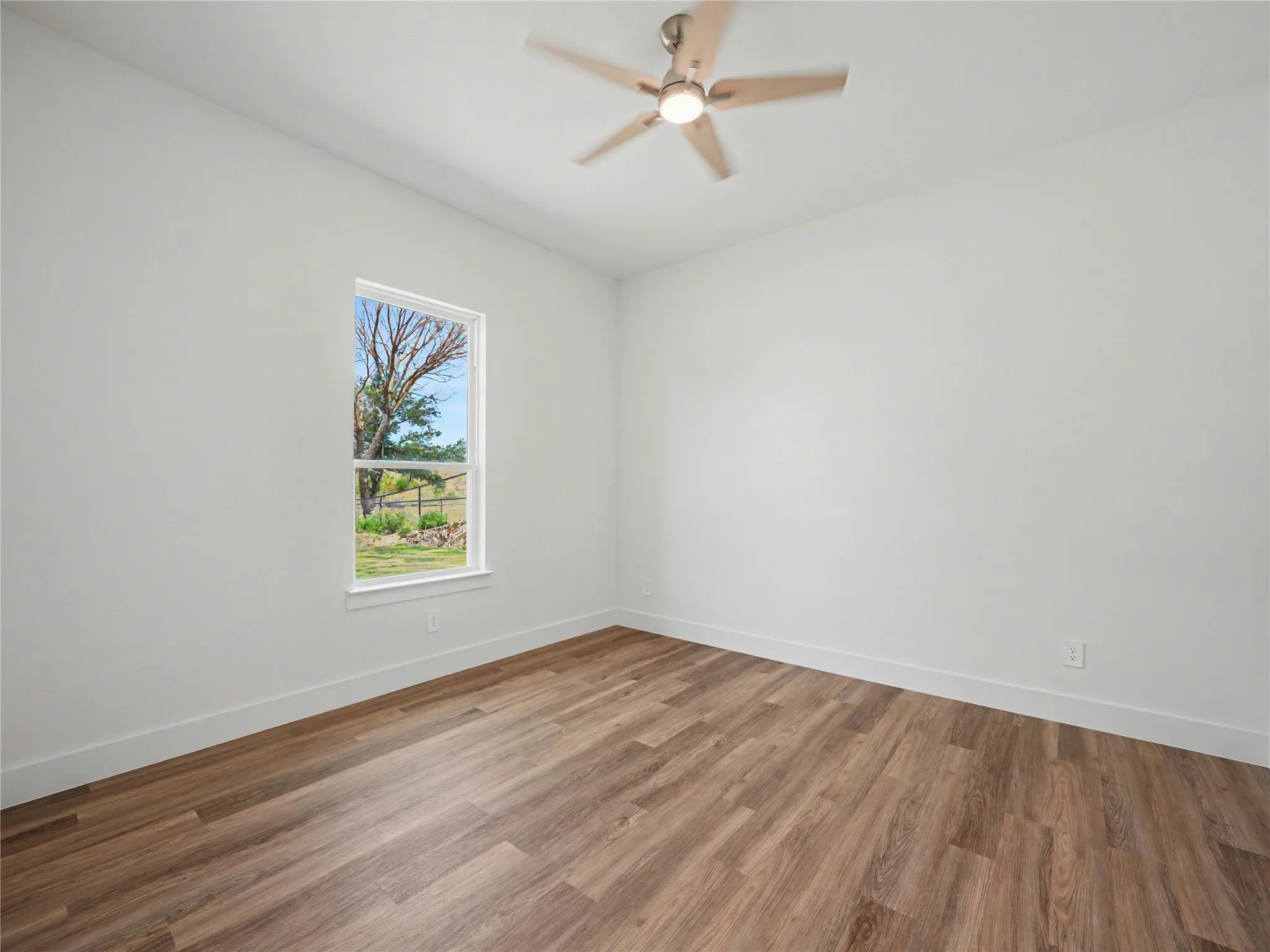 Room featuring wood-finish flooring, crisp white walls, and a contemporary ceiling fan