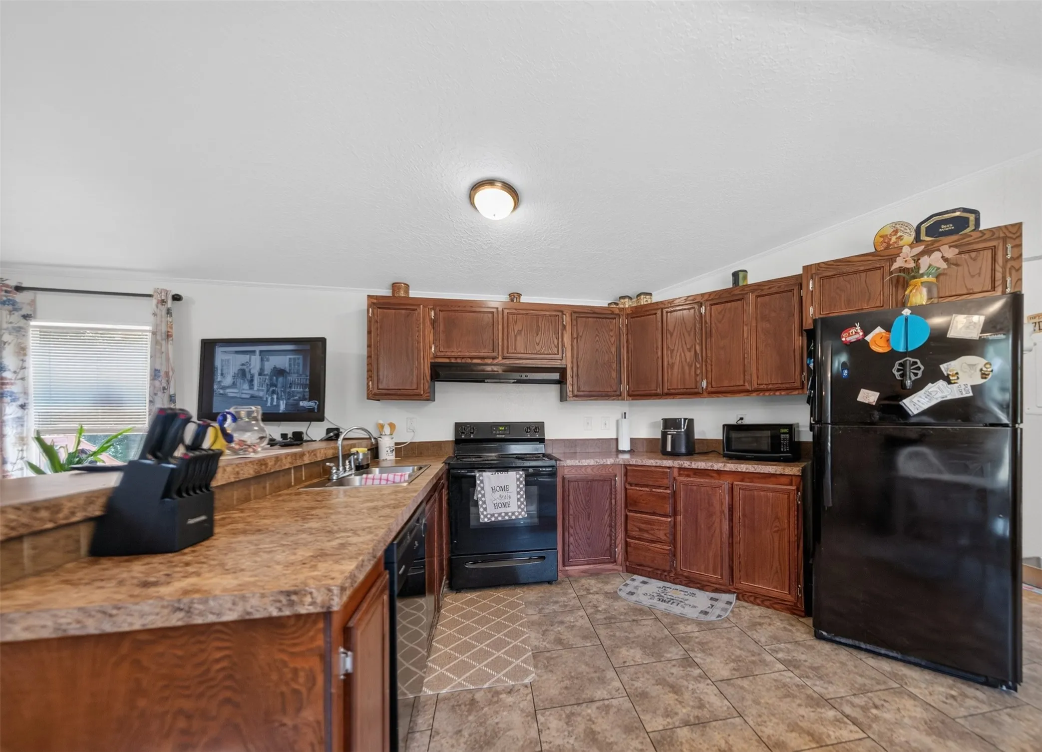Kitchen featuring ample wood cabinetry, patterned countertops, and black appliances including a built-in range and refrigerator