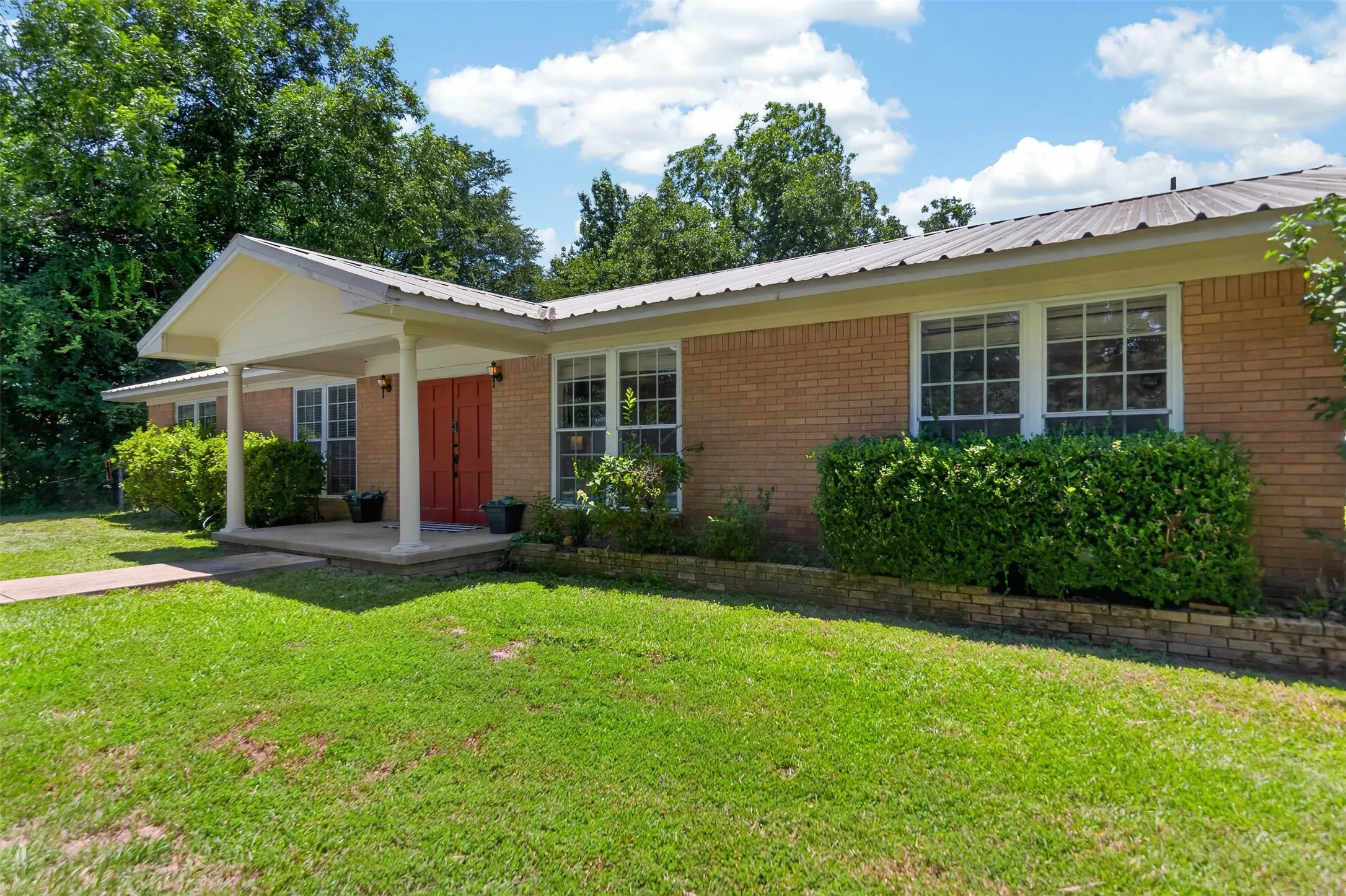 Brick exterior featuring a covered porch entry with white columns and a red front door