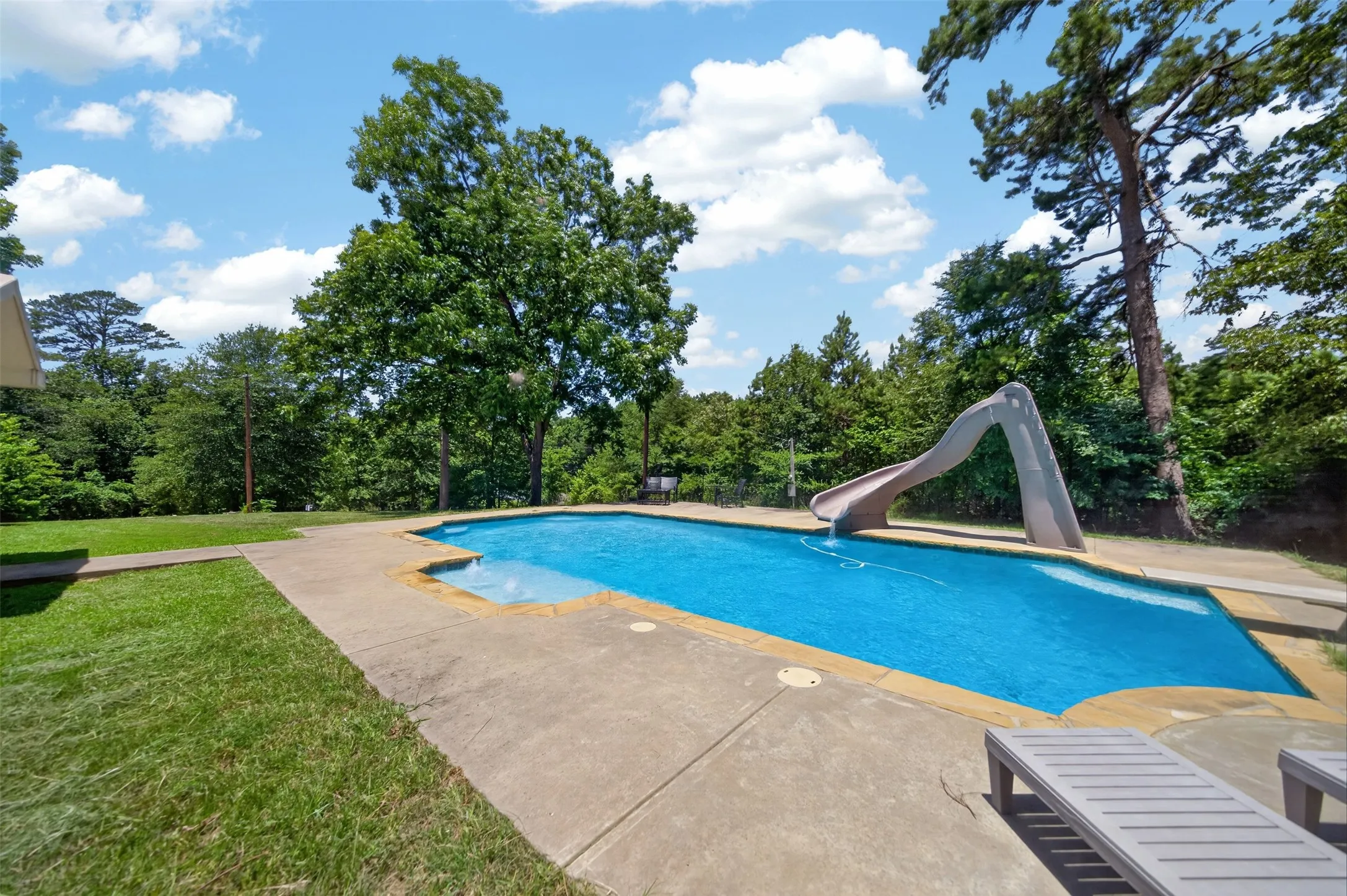 In-ground swimming pool with an integrated slide, surrounded by a concrete patio