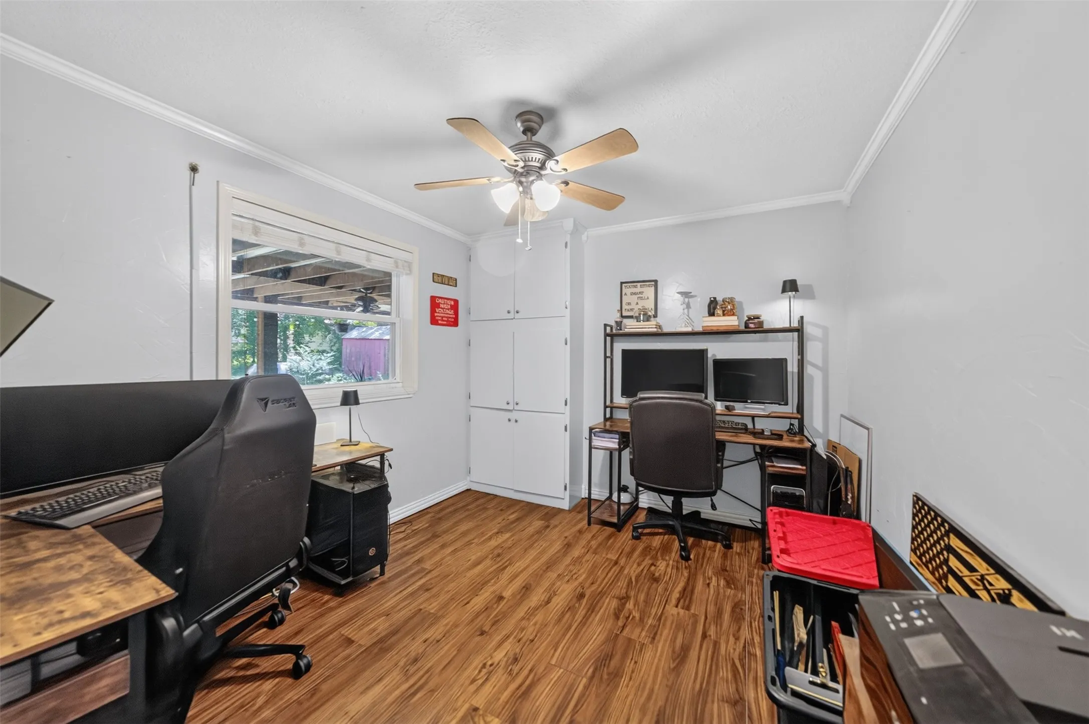 Room with wood-finish flooring, light grey walls, and white crown molding