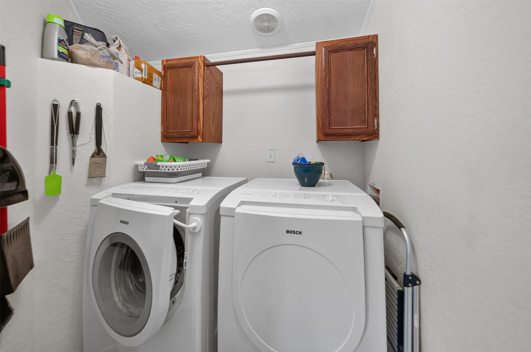 Dedicated utility area featuring white walls, overhead wood-finish cabinetry, and a high shelf for storage