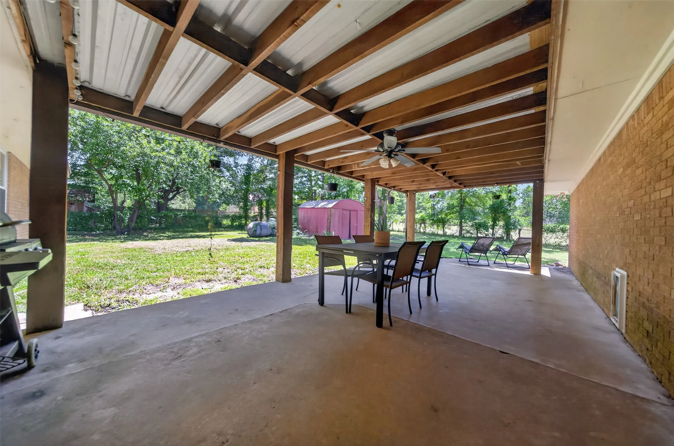 Expansive covered patio featuring a concrete surface and a wood-beamed ceiling with a mounted ceiling fan