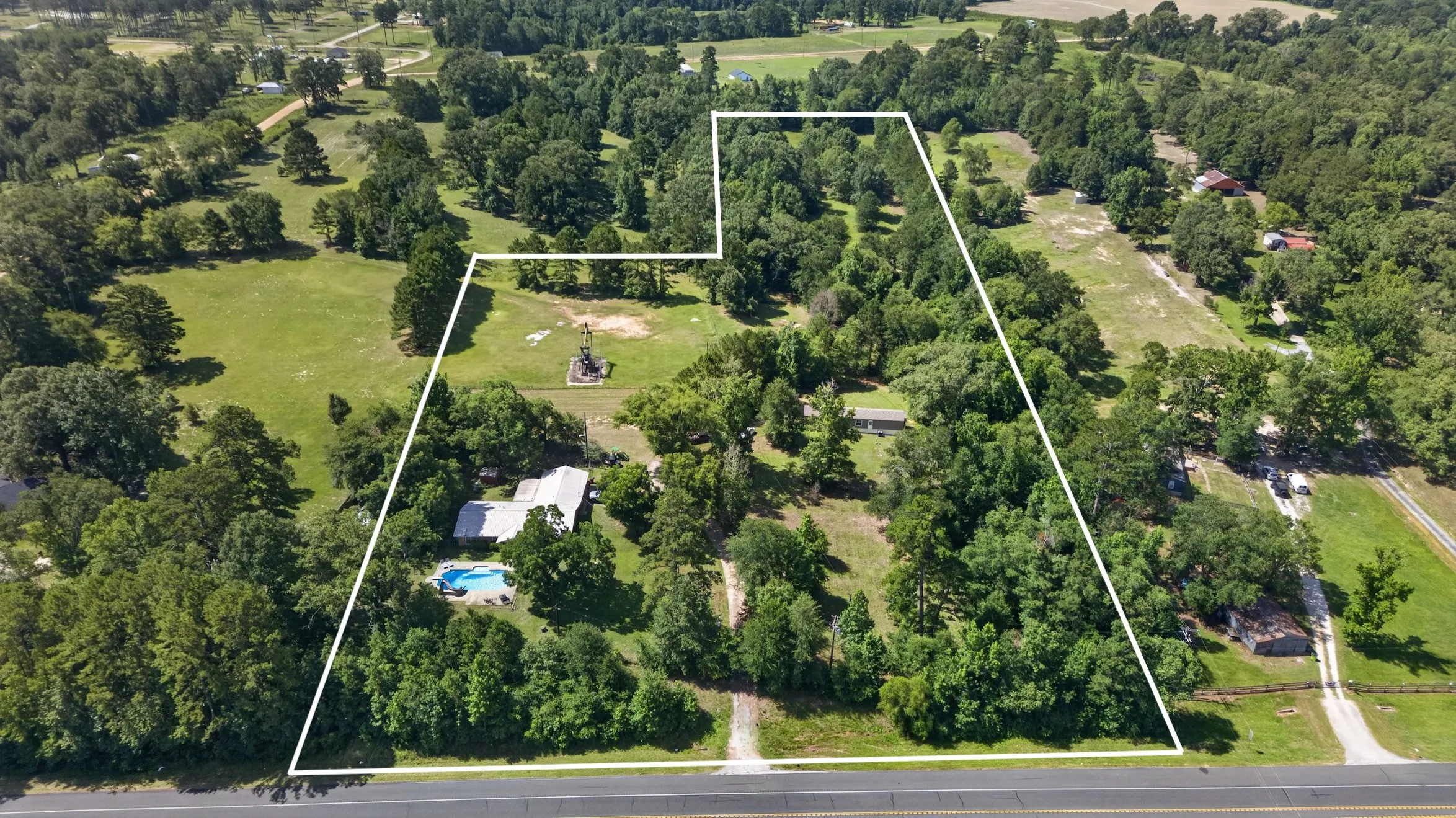 Expansive parcel featuring mature trees, open clearings, a single-story residence, a swimming pool, and direct road frontage