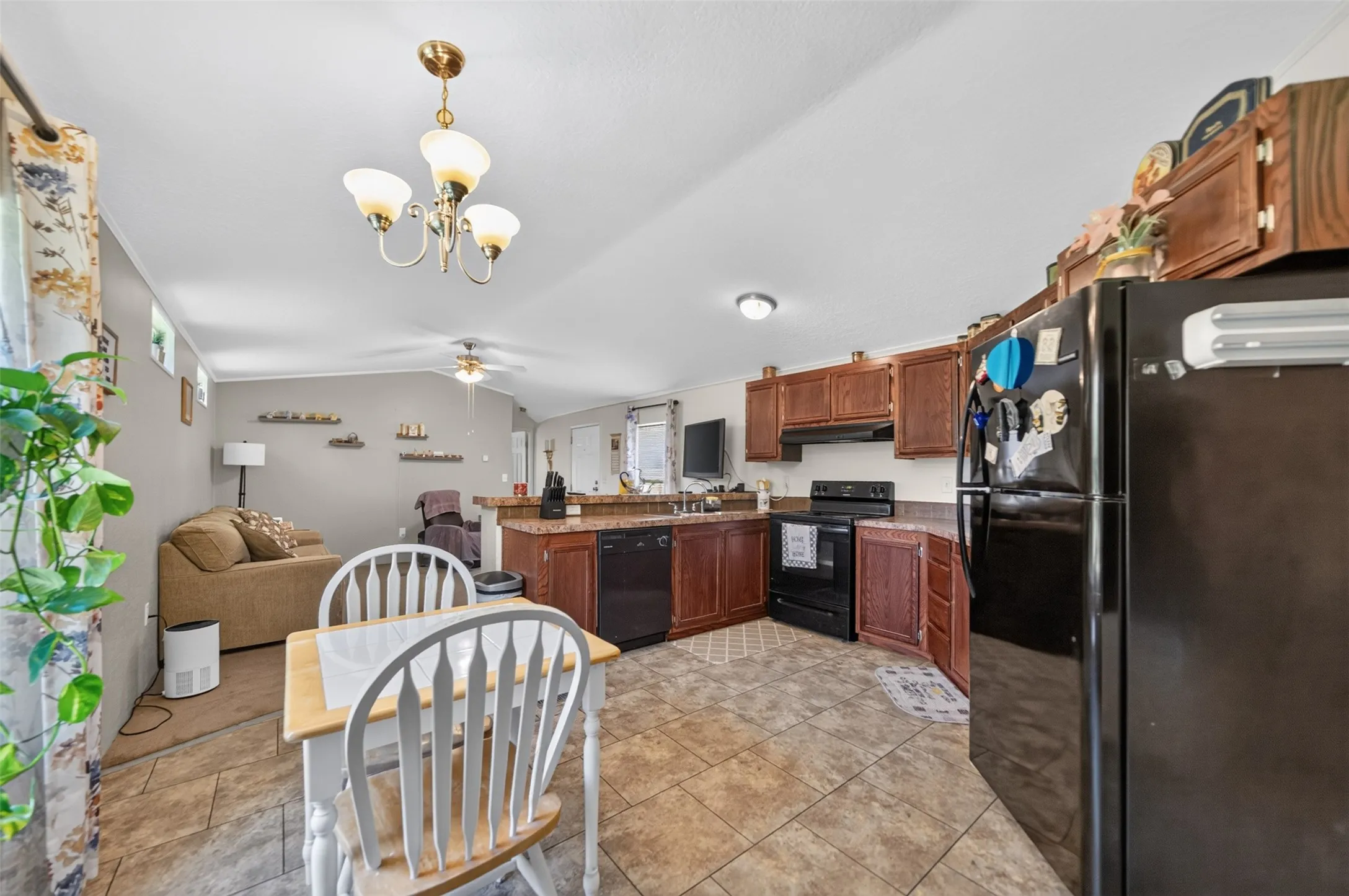 Open-concept kitchen and living area featuring dark wood-finish cabinetry, granite-style countertops, and a full suite of black appliances