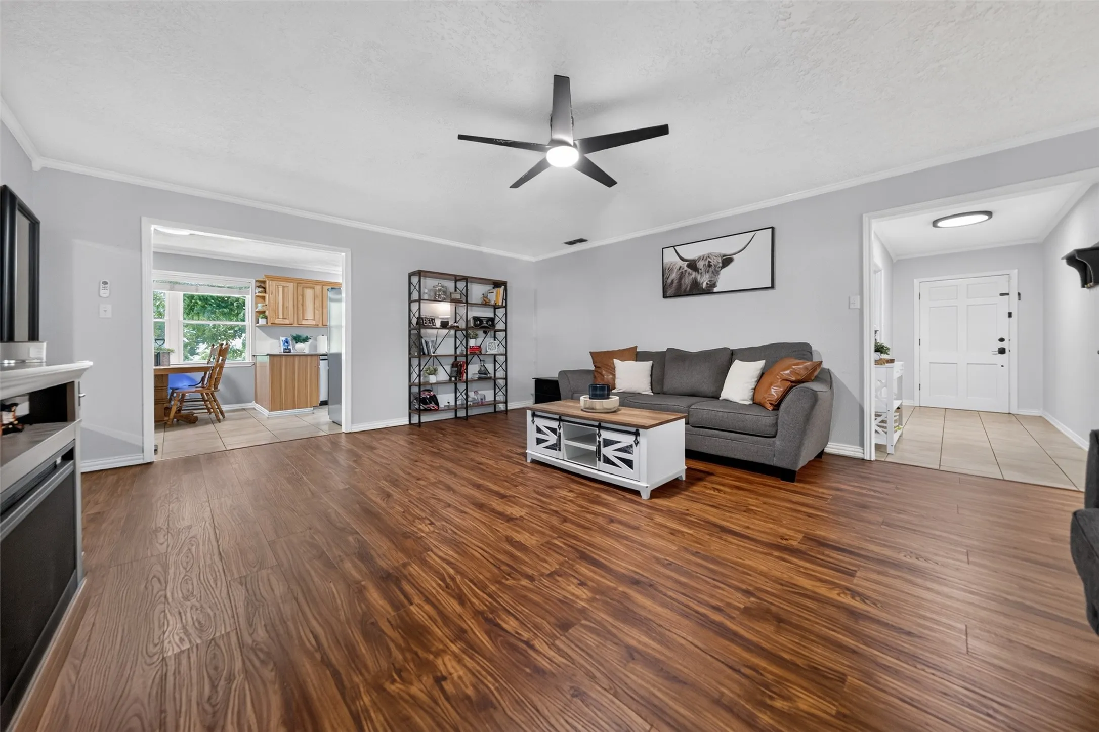 Open-concept living area featuring wood-finish flooring, a contemporary ceiling fan with integrated lighting, and crown molding