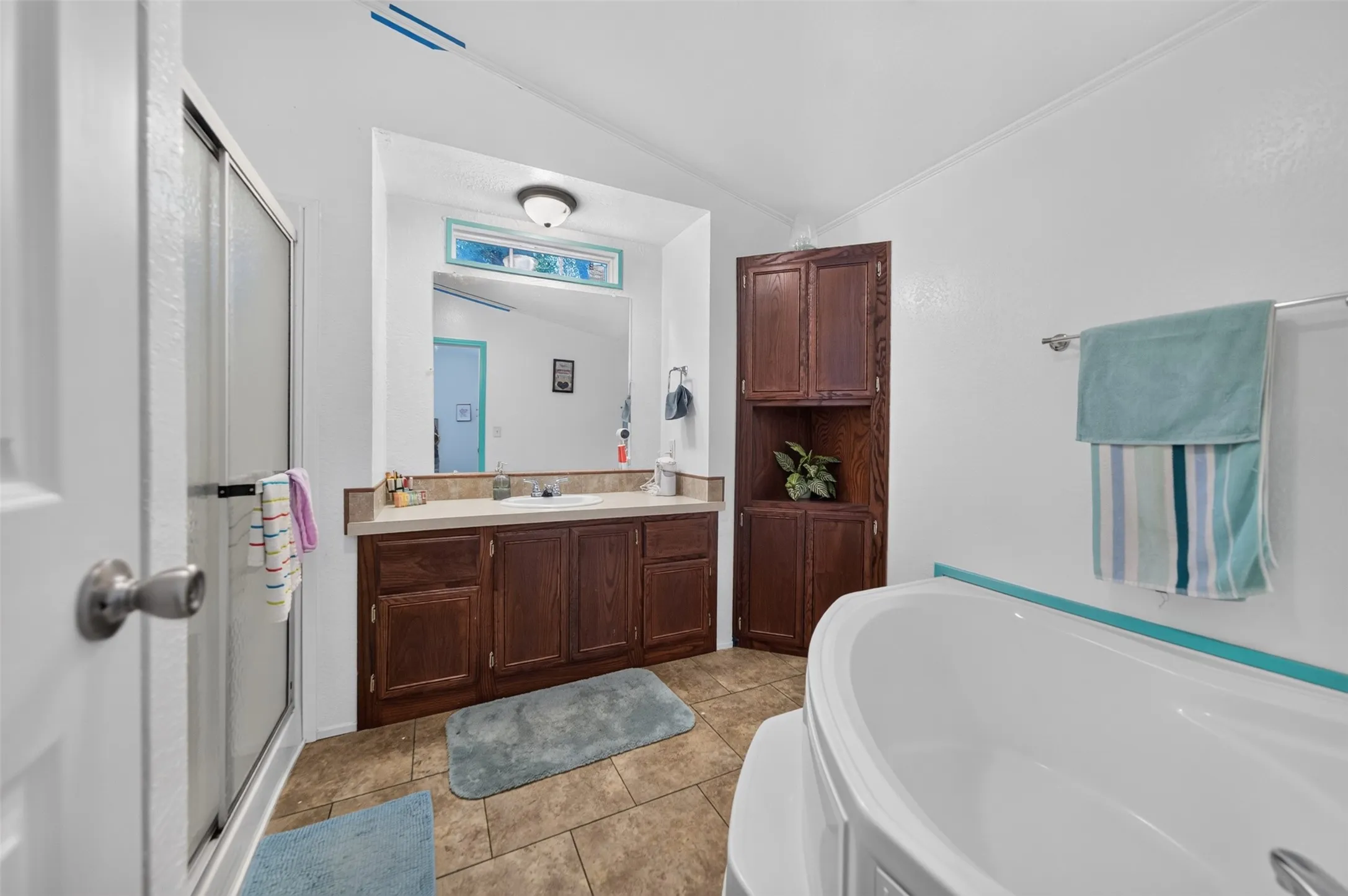 Bathroom featuring a freestanding tub, tiled shower with a glass enclosure, wood-finish vanity with an integrated sink, built-in wood-finish storage cabinetry, and ceramic tile flooring