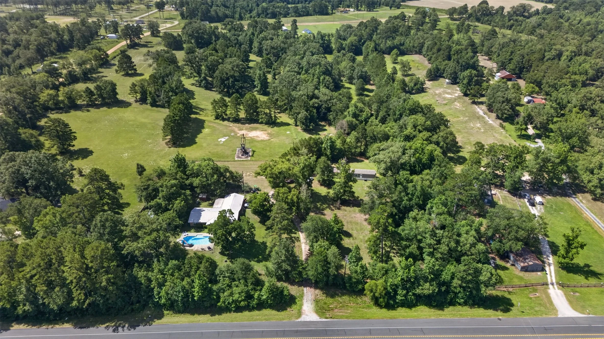 Expansive property featuring a main residence with a swimming pool, multiple outbuildings, wooded areas, and open fields