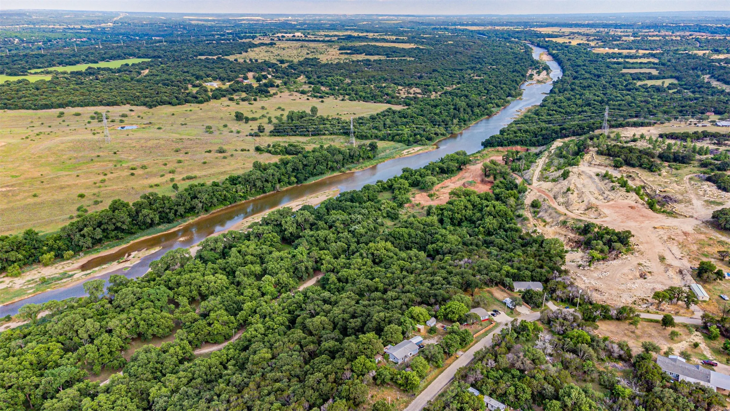 Aerial landscape featuring a winding river, dense riparian tree coverage, and surrounding open fields