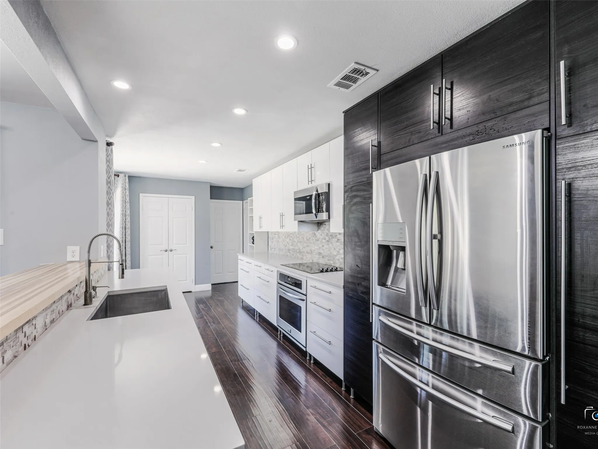 Modern updated kitchen featuring dark wood-finish flooring, quartz-style counters, stone backsplash and recessed lighting.  Fridge to convey with the property.