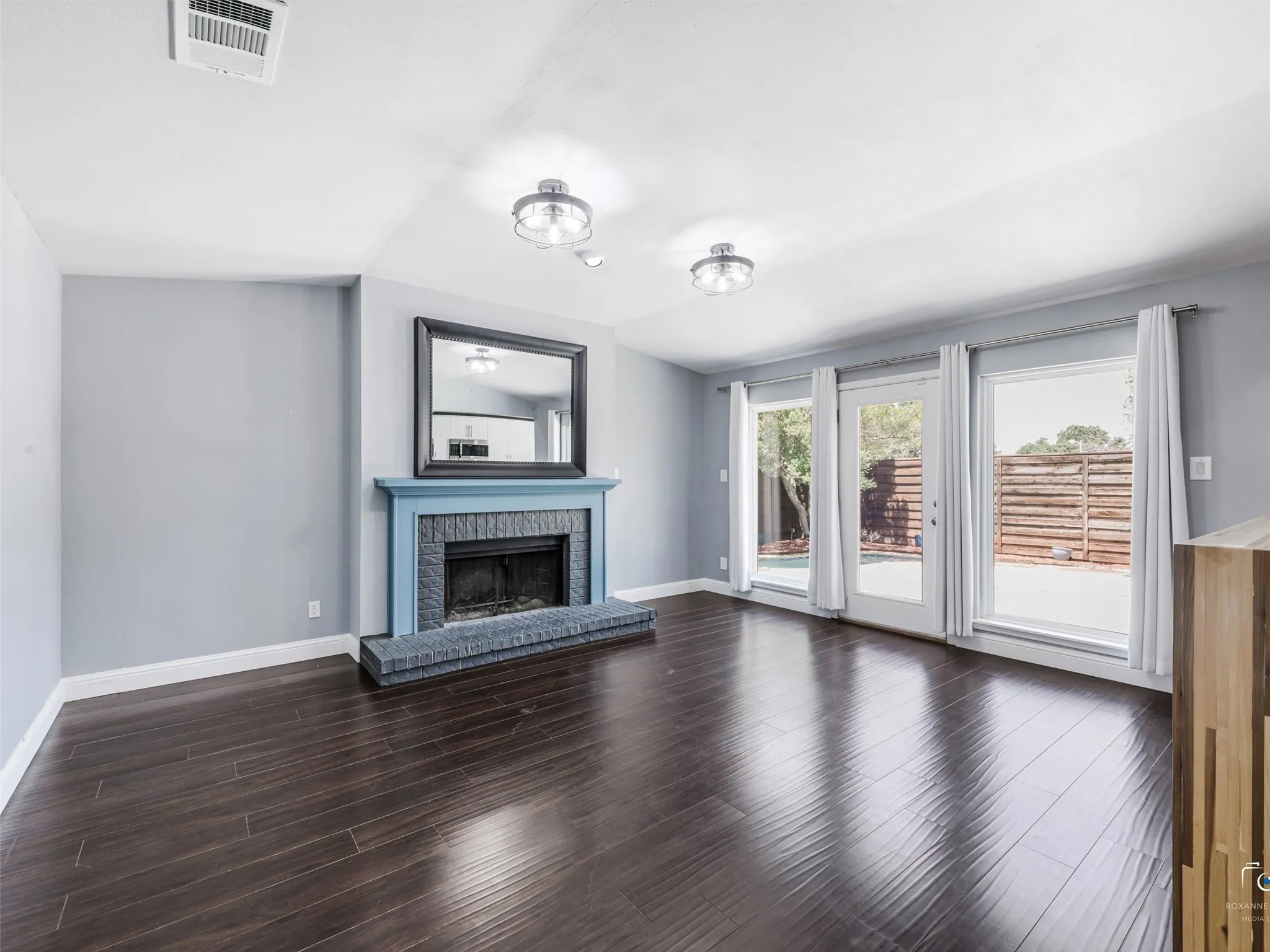 Living area featuring dark wood flooring, a fireplace with a blue mantel and dark tile surround, and two windows and a glass door opening to the backyard.