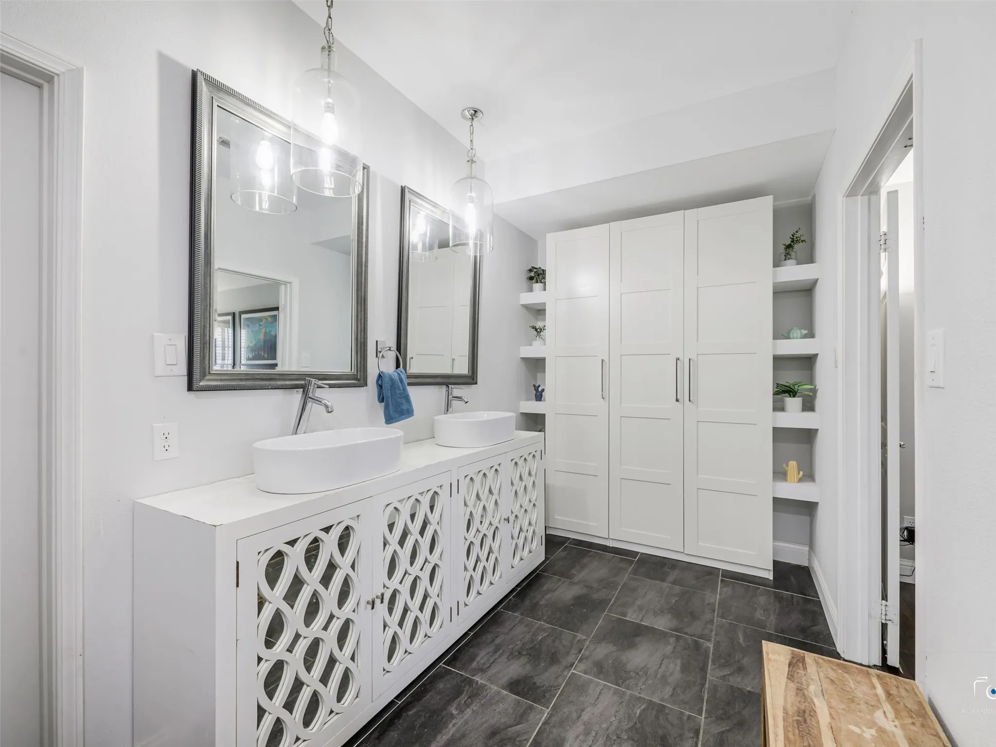 Bathroom featuring a dual vanity with vessel sinks, ornate cabinet fronts, pendant lighting, and a built-in storage unit with open shelving
