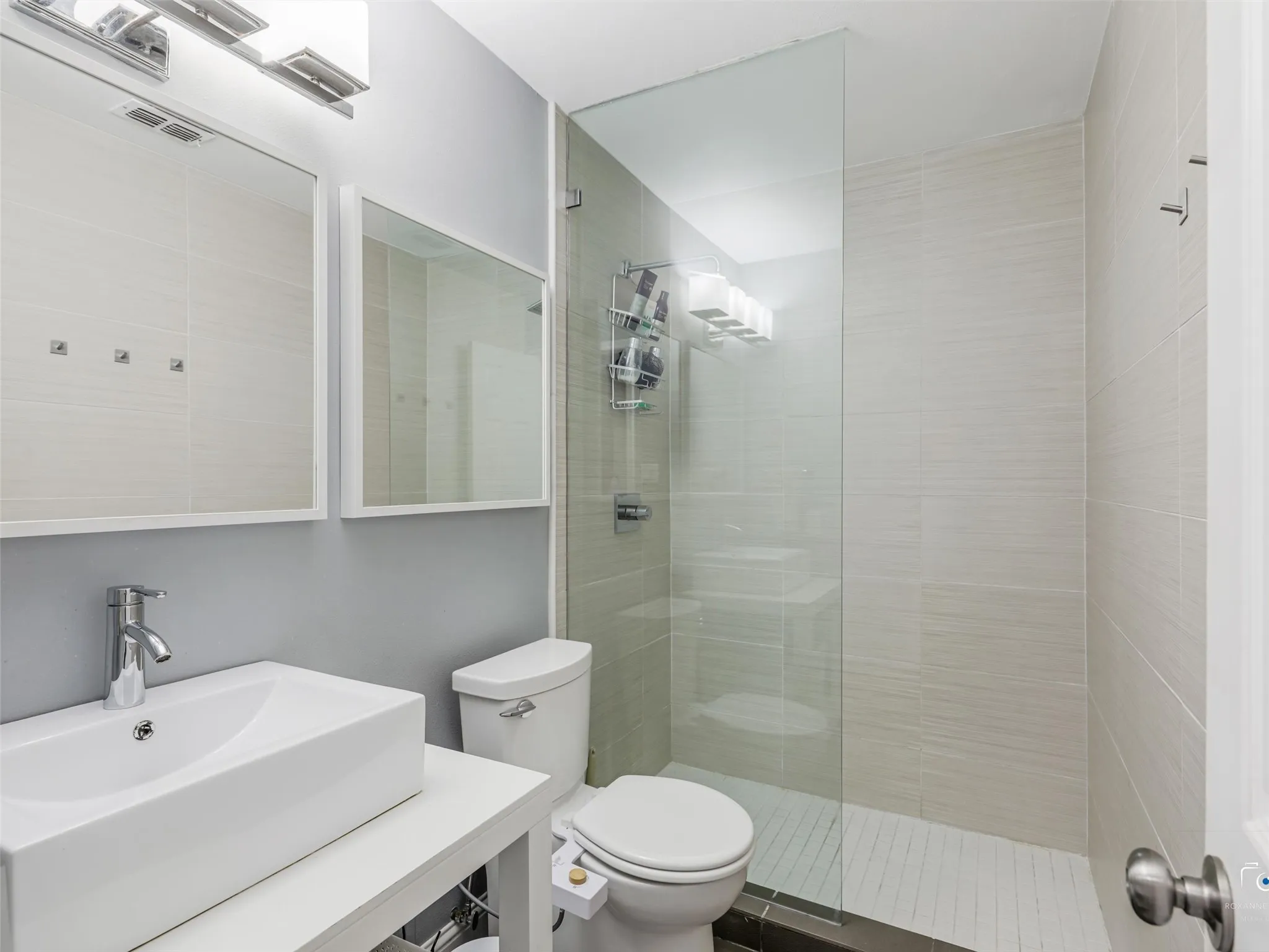 Bathroom two featuring a glass-enclosed shower, and floor to ceiling tile shower surround, and a rectangular vessel sink with a chrome faucet