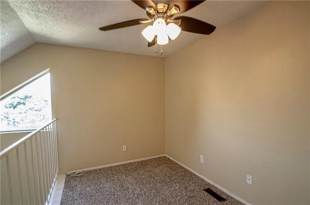 Carpeted loft space featuring an angled wall with a triangular window, a ceiling fan with integrated lighting, and a white metal railing