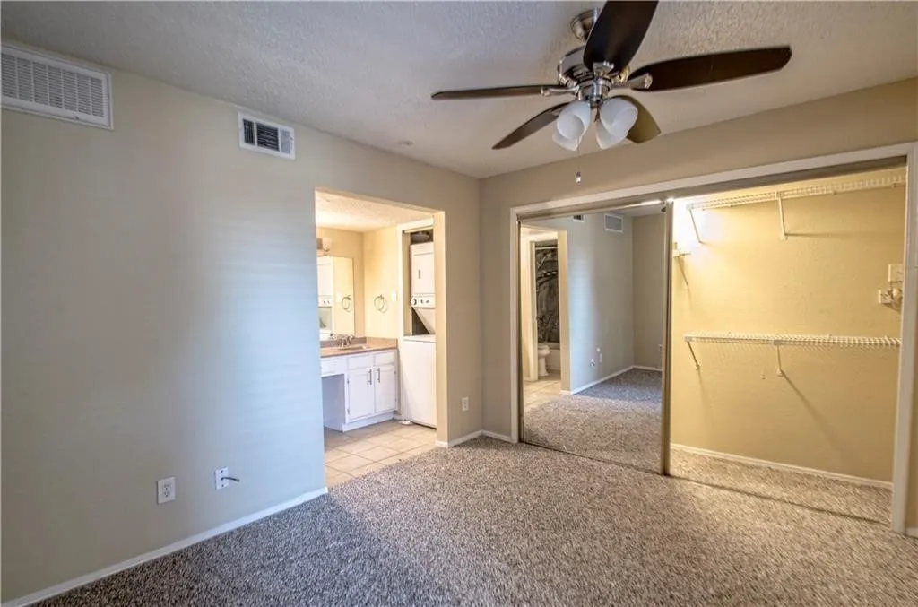 Carpeted room with a ceiling fan, mirrored closet doors, and an en-suite vanity area with tile flooring and a built-in washer/dryer unit