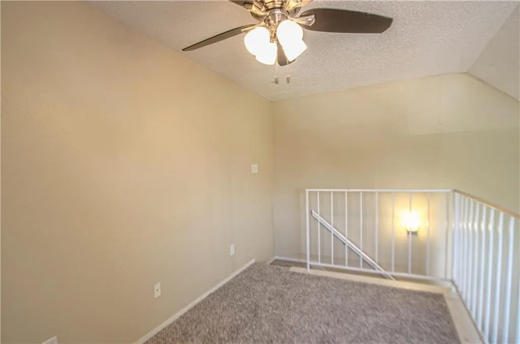 Carpeted loft area featuring a ceiling fan with integrated lighting, textured walls, and a white metal railing