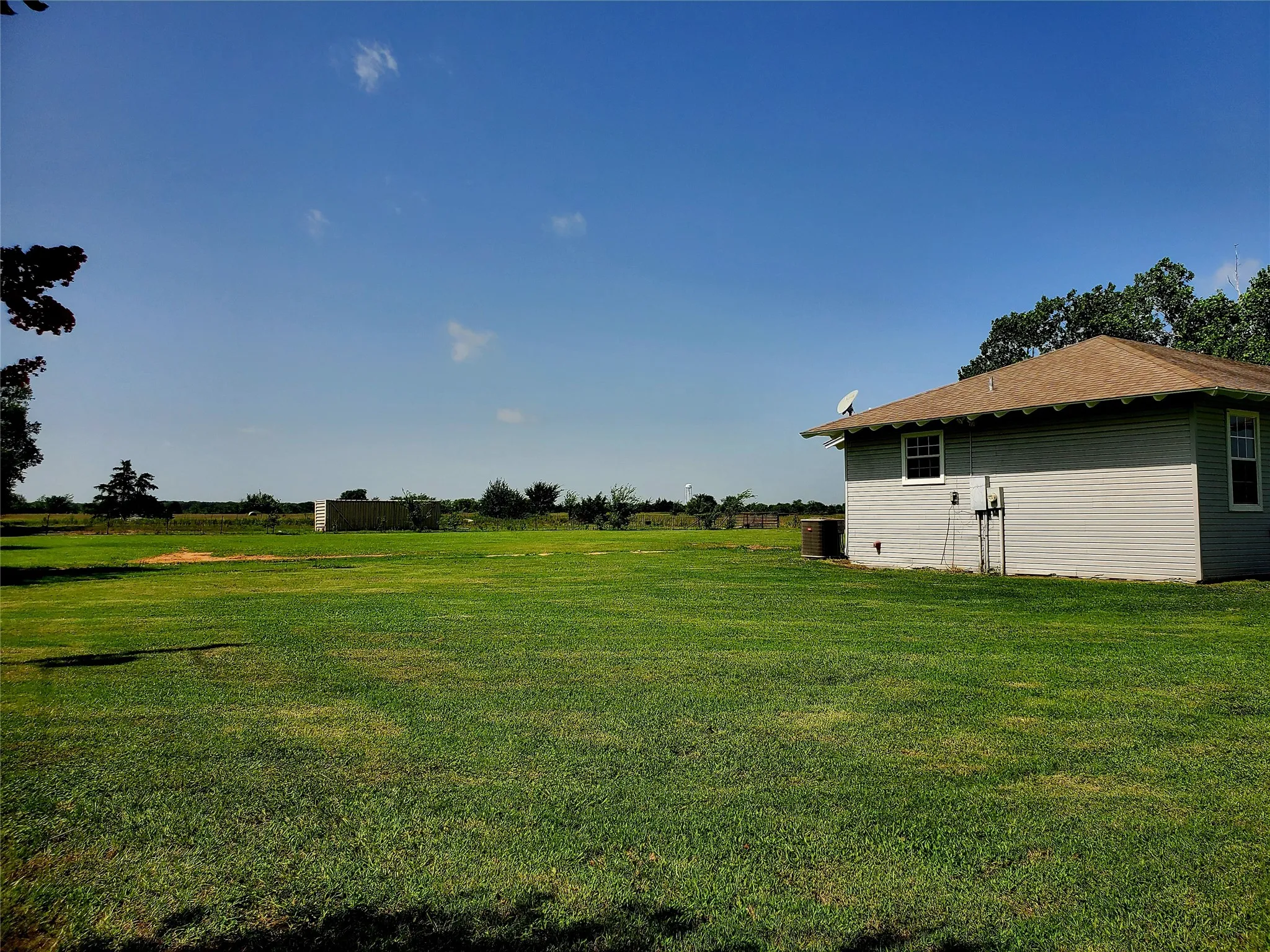 Expansive green lawn bordering a property with siding exterior and a gabled roof