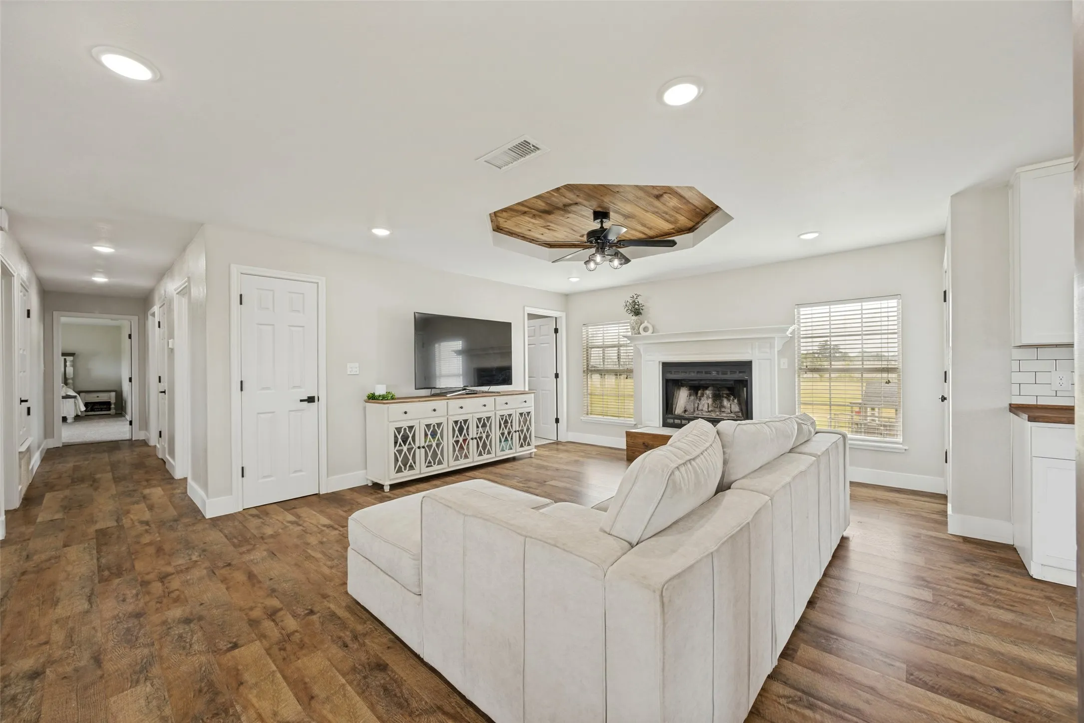 Open-concept living space featuring wood-finish flooring, recessed lighting, and a decorative ceiling fan with a wood-planked octagonal tray ceiling