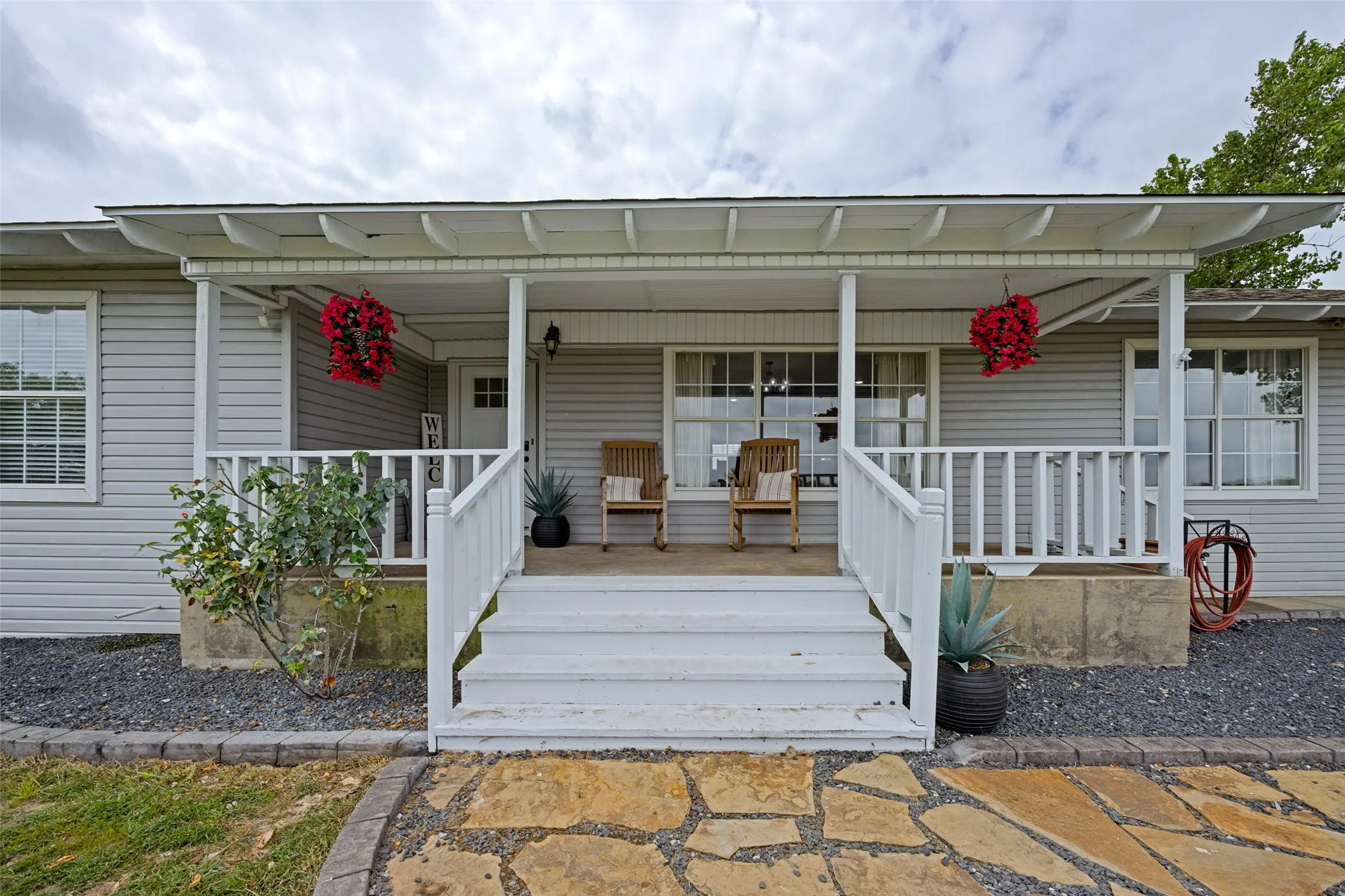 Front porch with white railing, light gray siding, multiple windows, and a flagstone pathway