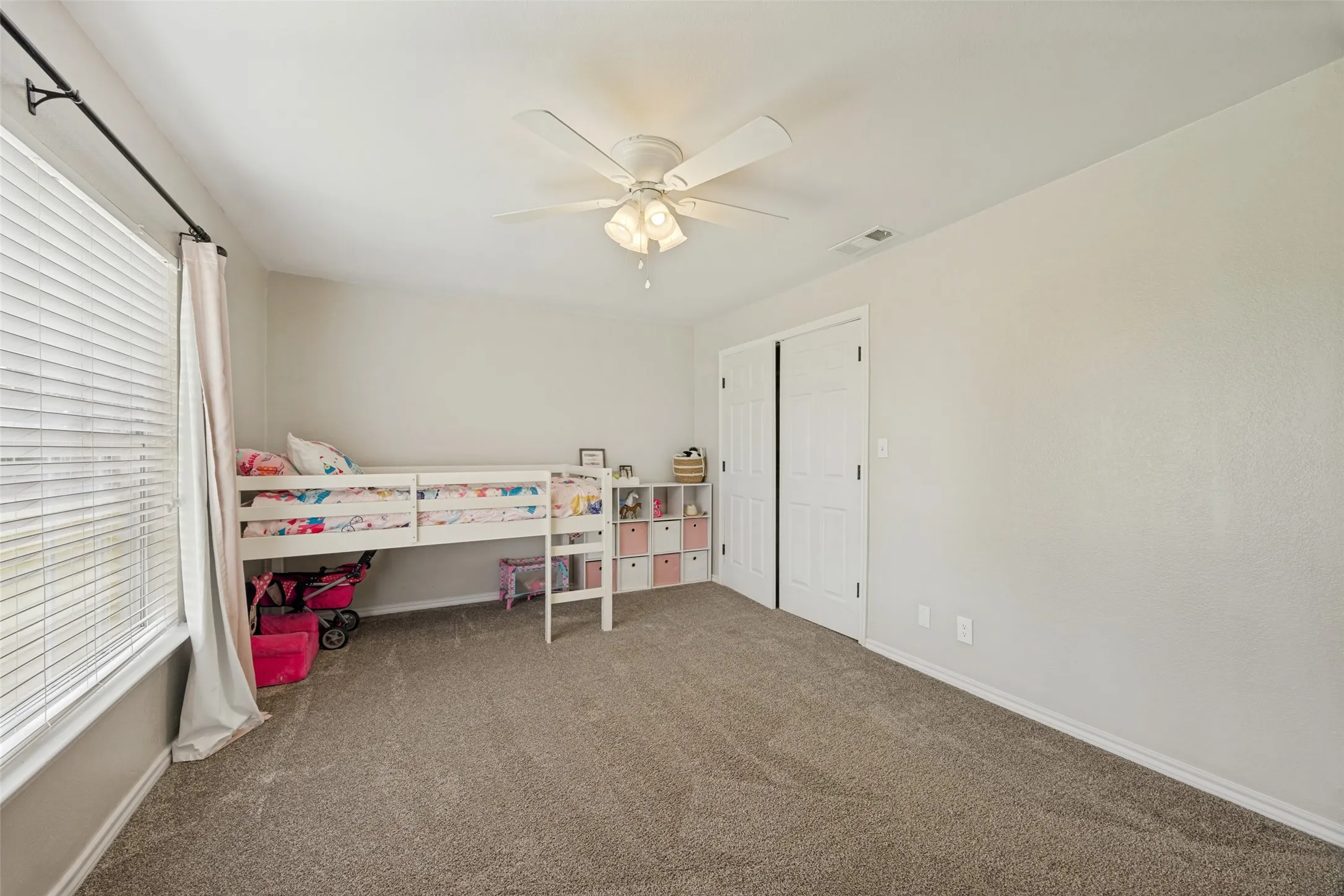 Carpeted room featuring a ceiling fan with light fixture, window with blinds, and white bi-fold closet doors