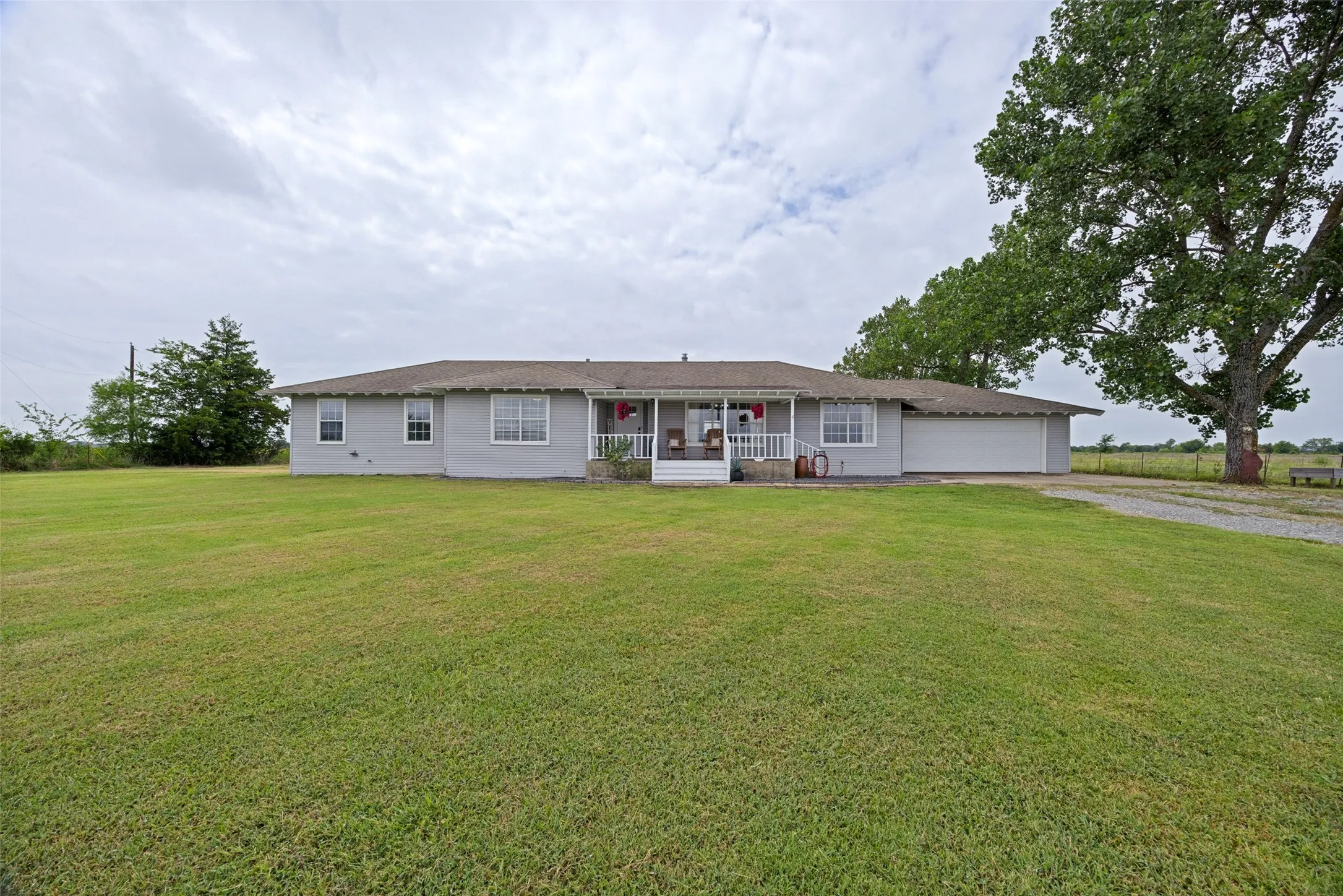 Ranch-style residence featuring a covered front porch with white railings, a gravel driveway, and a two-car garage