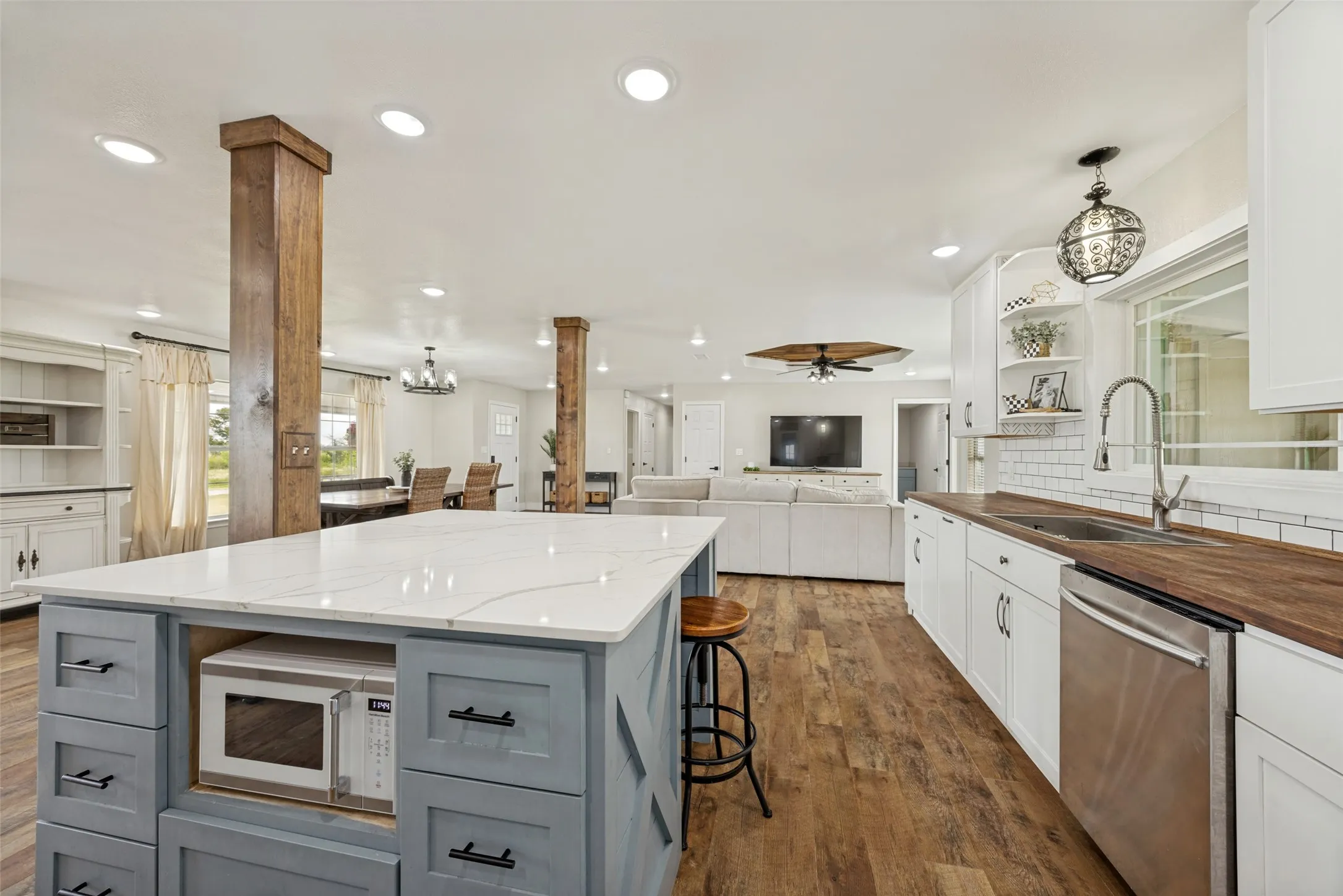 Kitchen featuring a large island with a quartz countertop and integrated microwave, wood-finish flooring, white cabinetry, a subway tile backsplash, and a stainless steel dishwasher