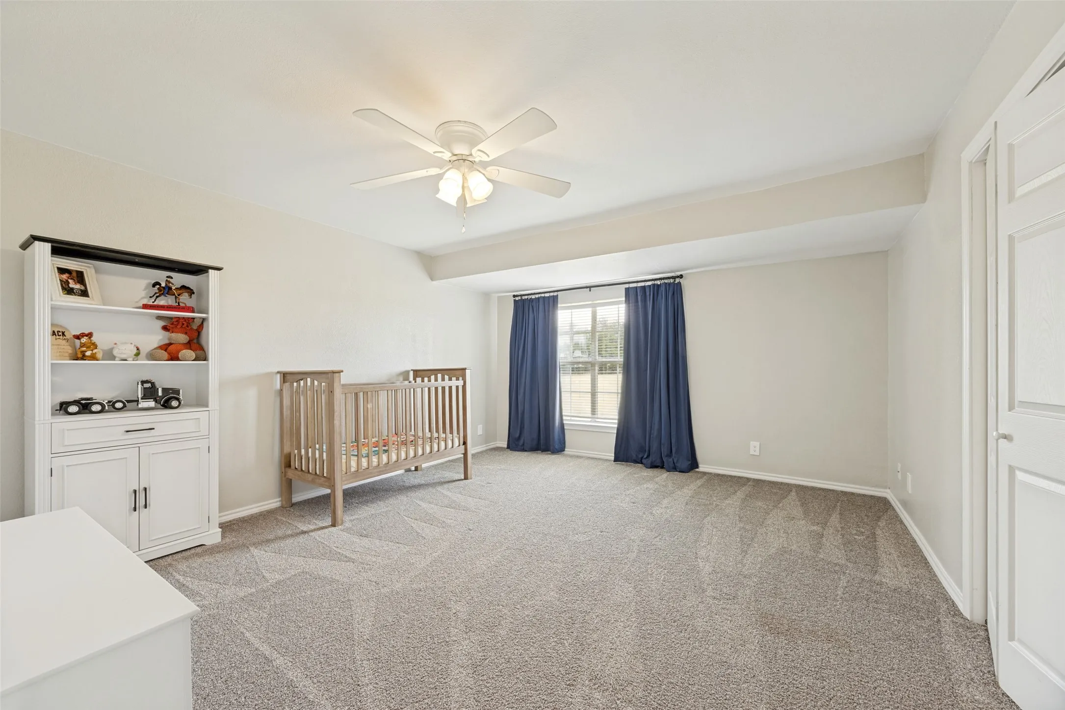 Spacious carpeted room featuring a ceiling fan with light fixture, large window, vaulted ceiling, and a paneled interior door