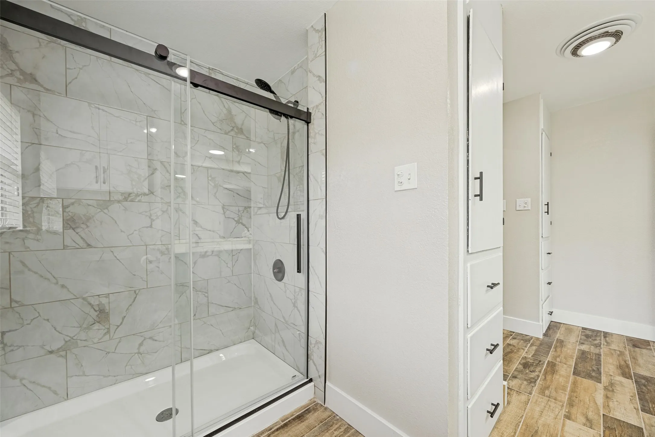 Walk-in shower featuring a sliding glass door, white marble-style tiled walls, and matte black hardware