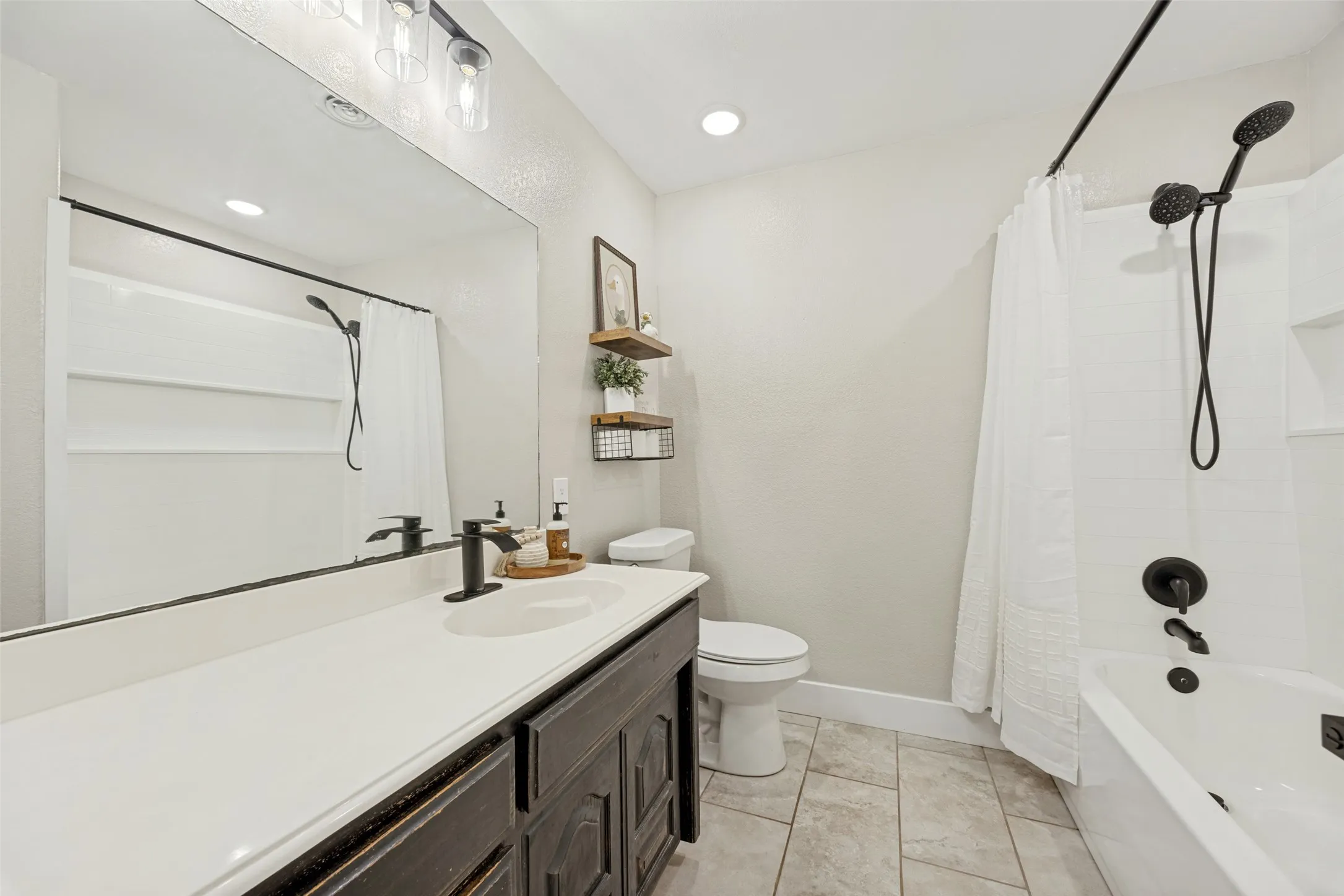 Bathroom featuring a dark wood-finish vanity with a white countertop, large mirror, and black fixtures