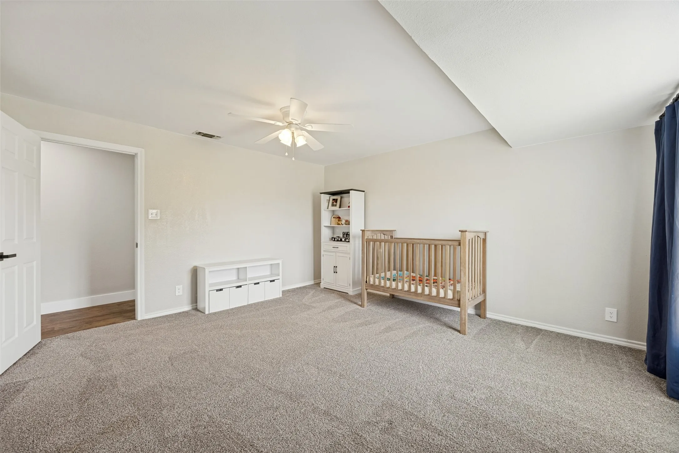 Carpeted room with a ceiling fan, white baseboards, and a white door with black hardware