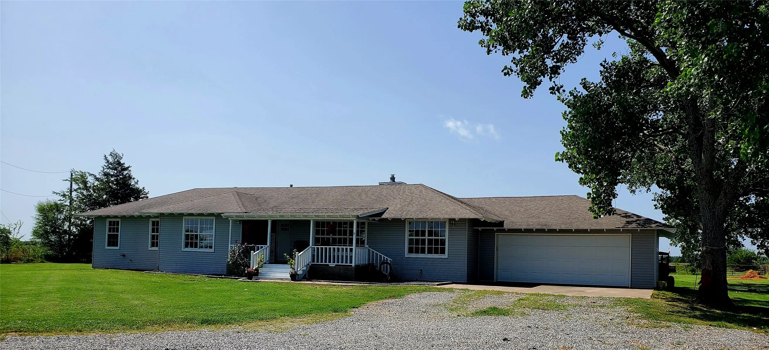 Single-story home featuring a covered front porch with white railings, a two-car garage, and a gravel driveway