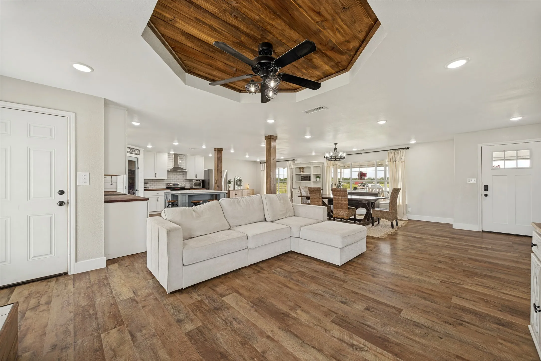 Open-concept living area featuring wood-finish flooring, recessed lighting, and a prominent wood-clad ceiling detail with a ceiling fan