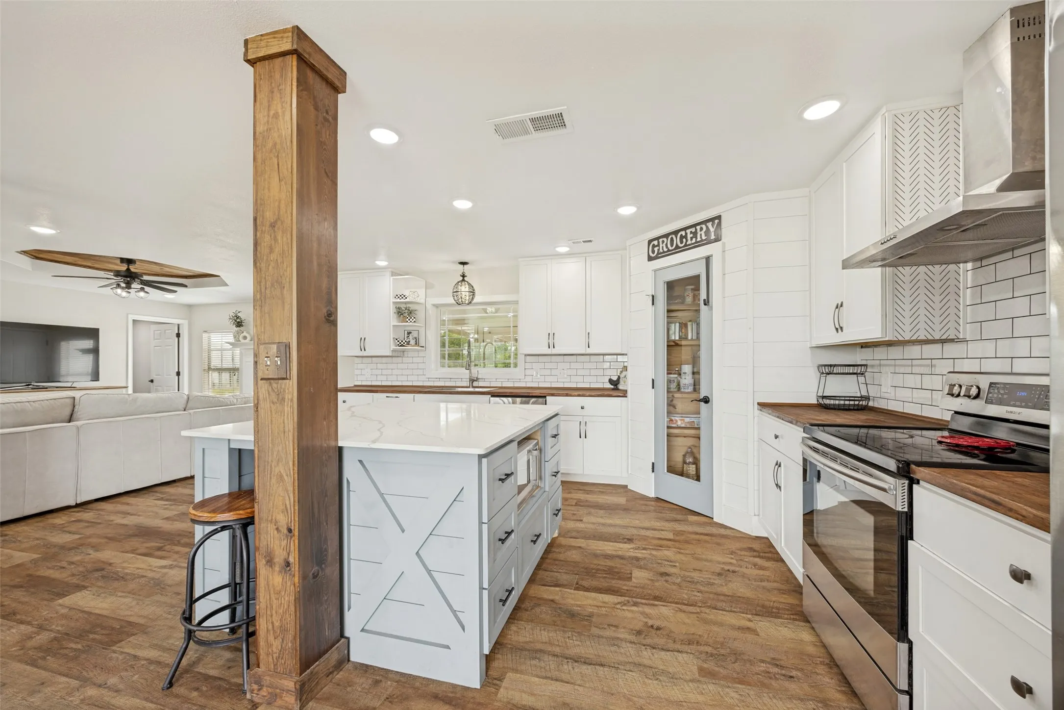 Kitchen featuring a central island with a quartz countertop and integrated storage, wood-finish flooring, white cabinetry, a subway tile backsplash, and a pantry with a glass-paned door