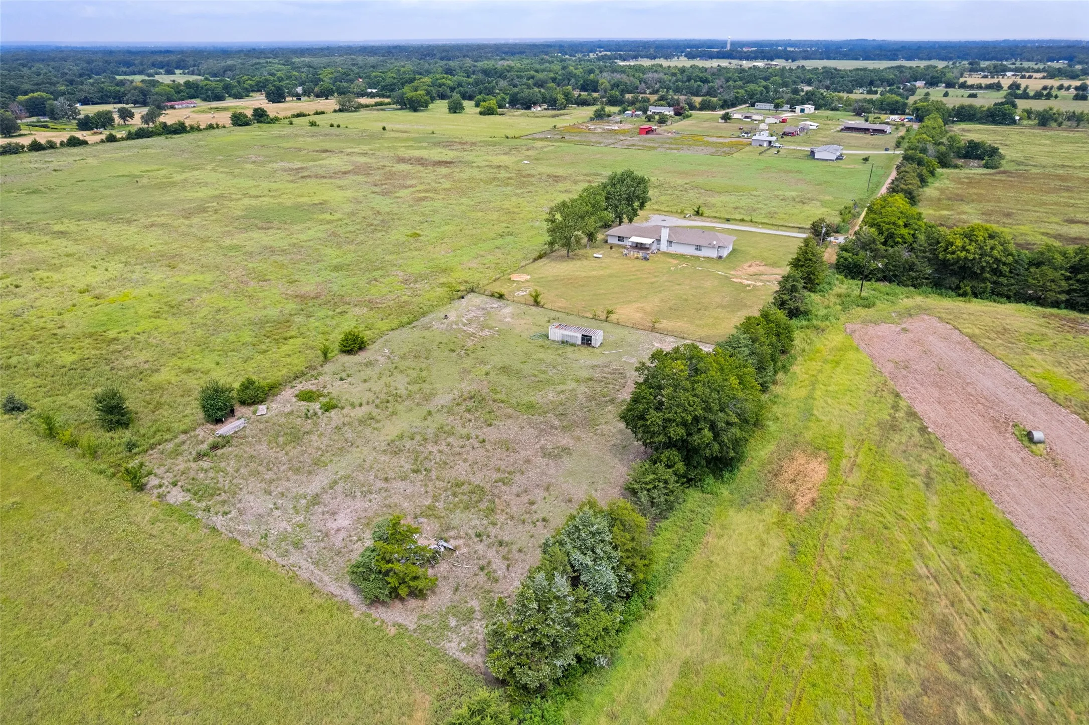 Expansive rural landscape featuring a single-story residence, a detached shed, a fenced perimeter, scattered trees, and vast open acreage