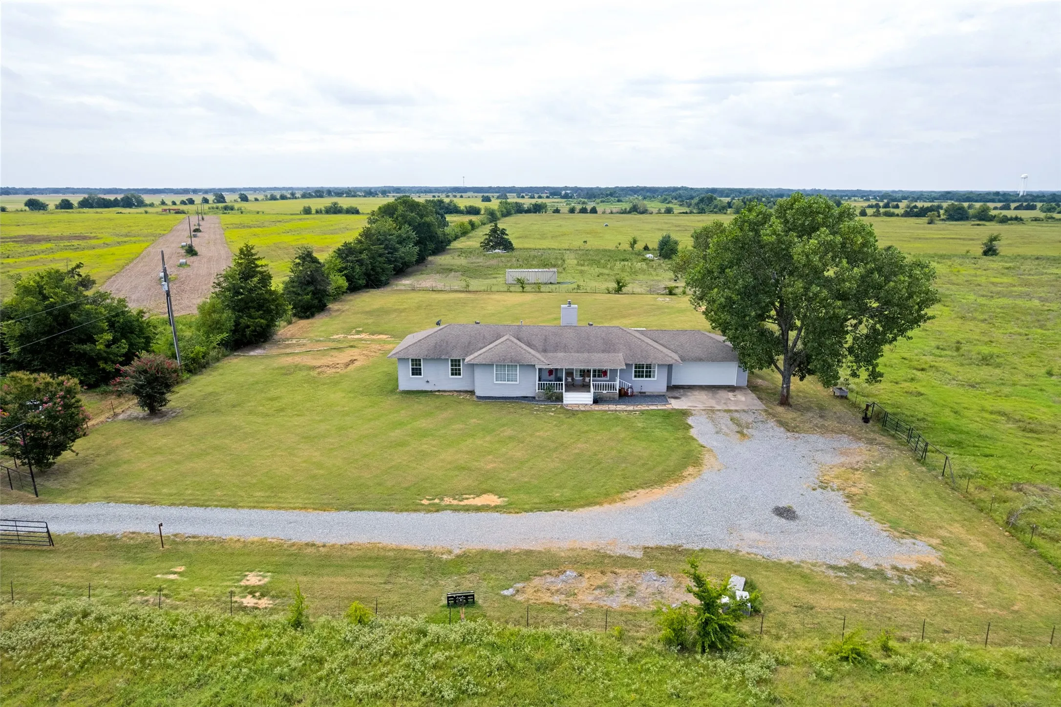 Ranch-style residence featuring a gravel driveway, front porch, mature trees, and an expansive surrounding landscape