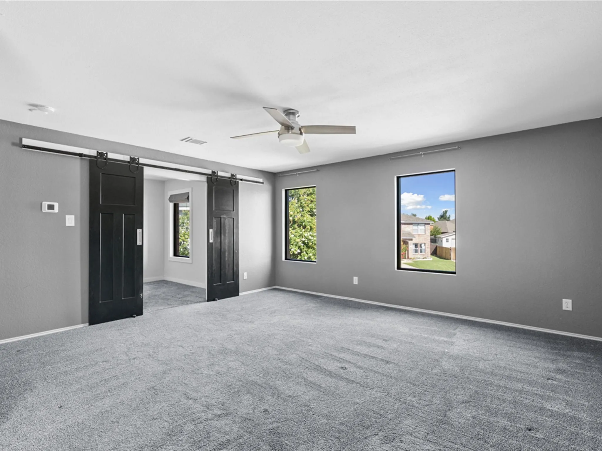 Unfurnished bedroom featuring a barn door, carpet flooring, and a ceiling fan
