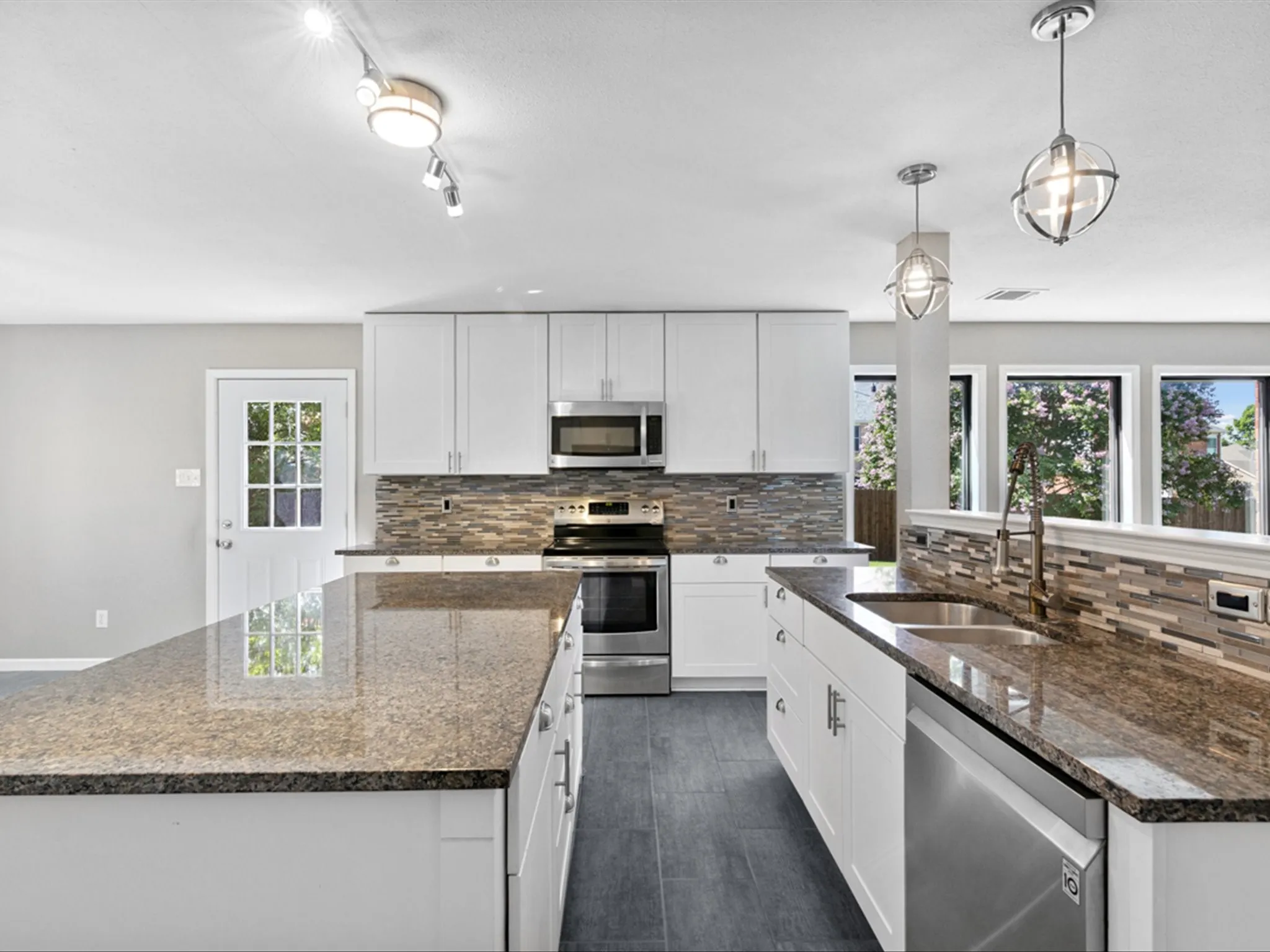Kitchen featuring stainless steel appliances, an island with sink, tasteful backsplash, and dark stone countertops