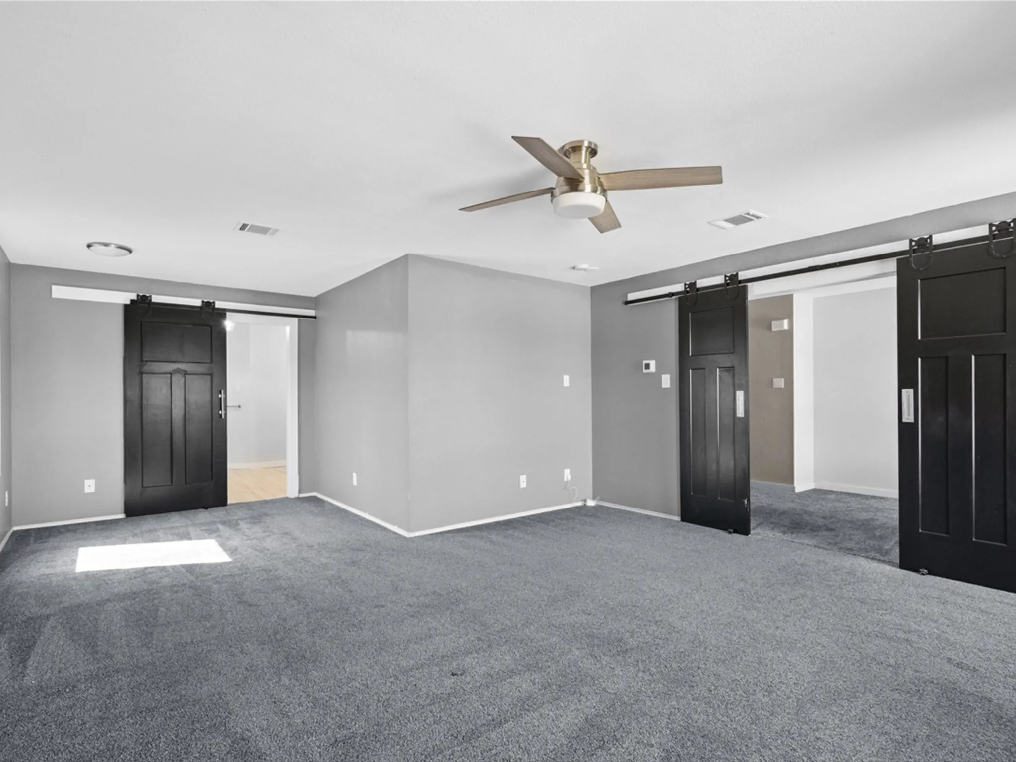 Unfurnished bedroom featuring a barn door, carpet, and ceiling fan