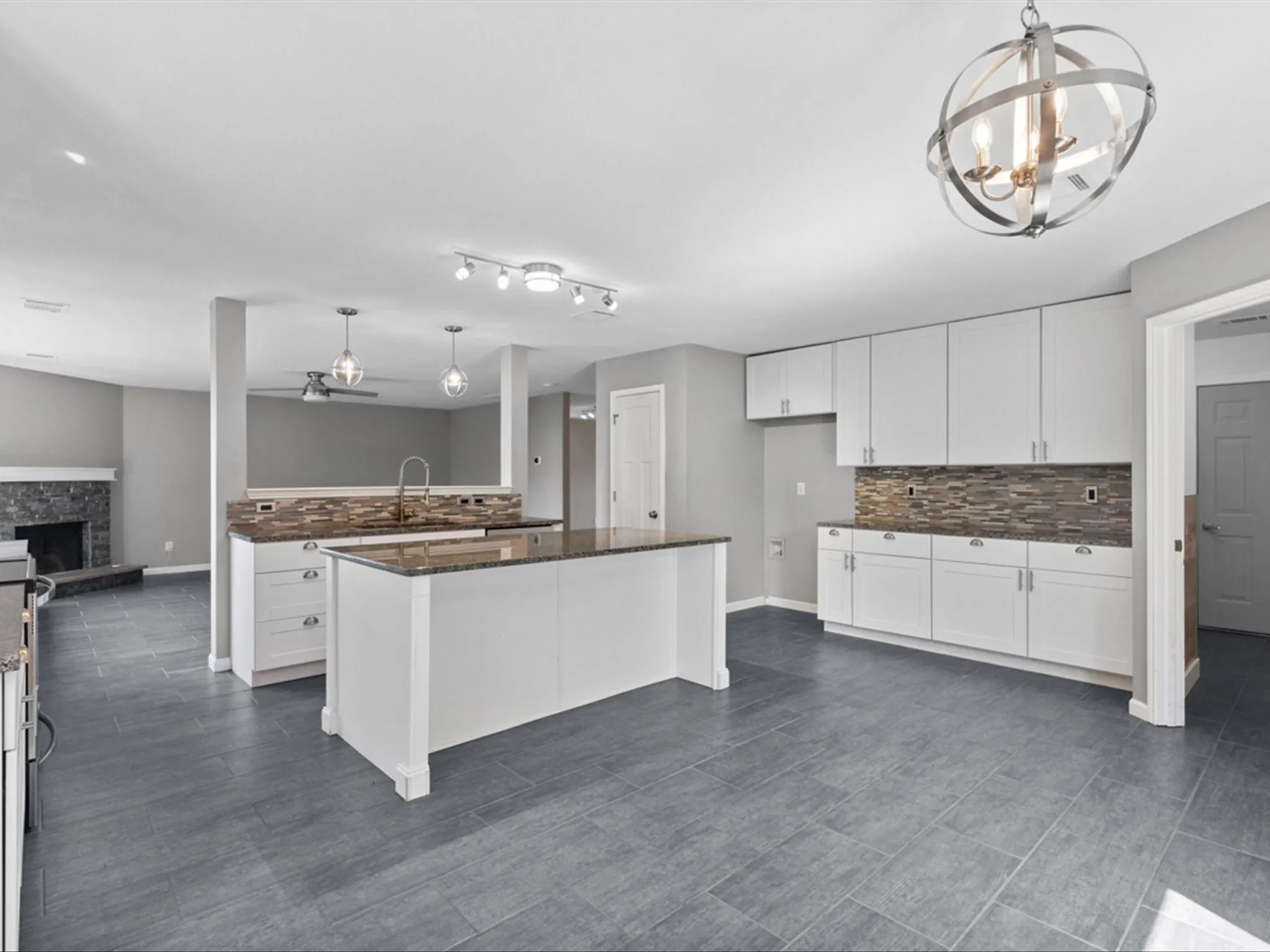 Kitchen featuring decorative backsplash, white cabinets, a chandelier, a fireplace, and hanging light fixtures