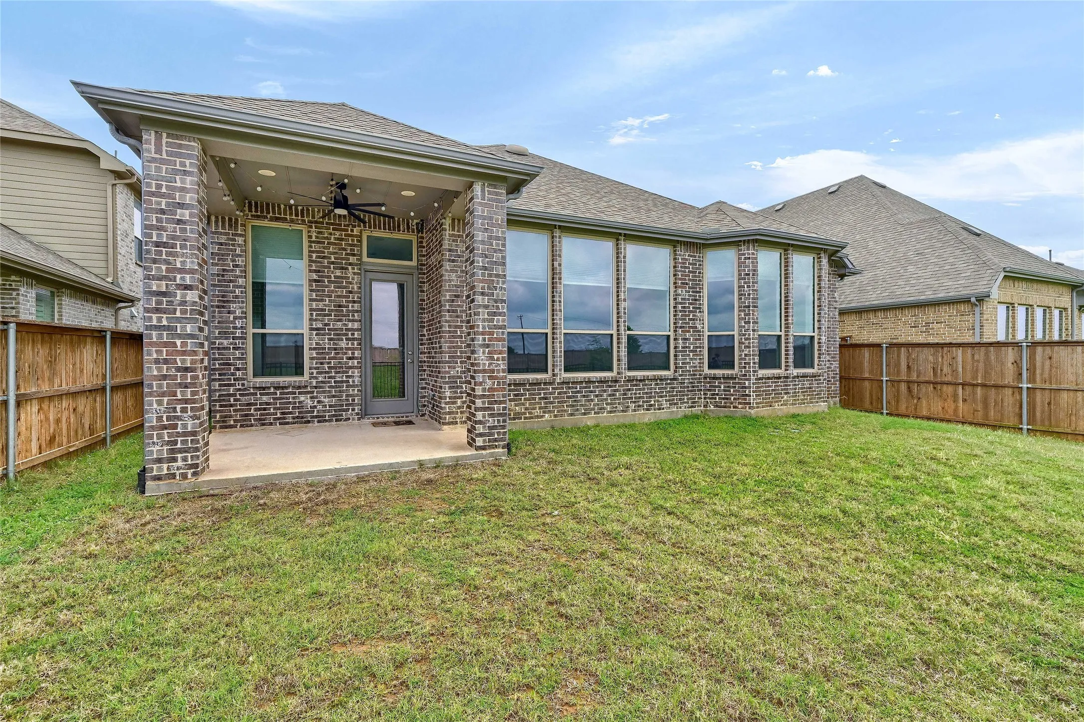 Rear view of property featuring a ceiling fan, a patio area, brick siding, a fenced backyard, and a yard